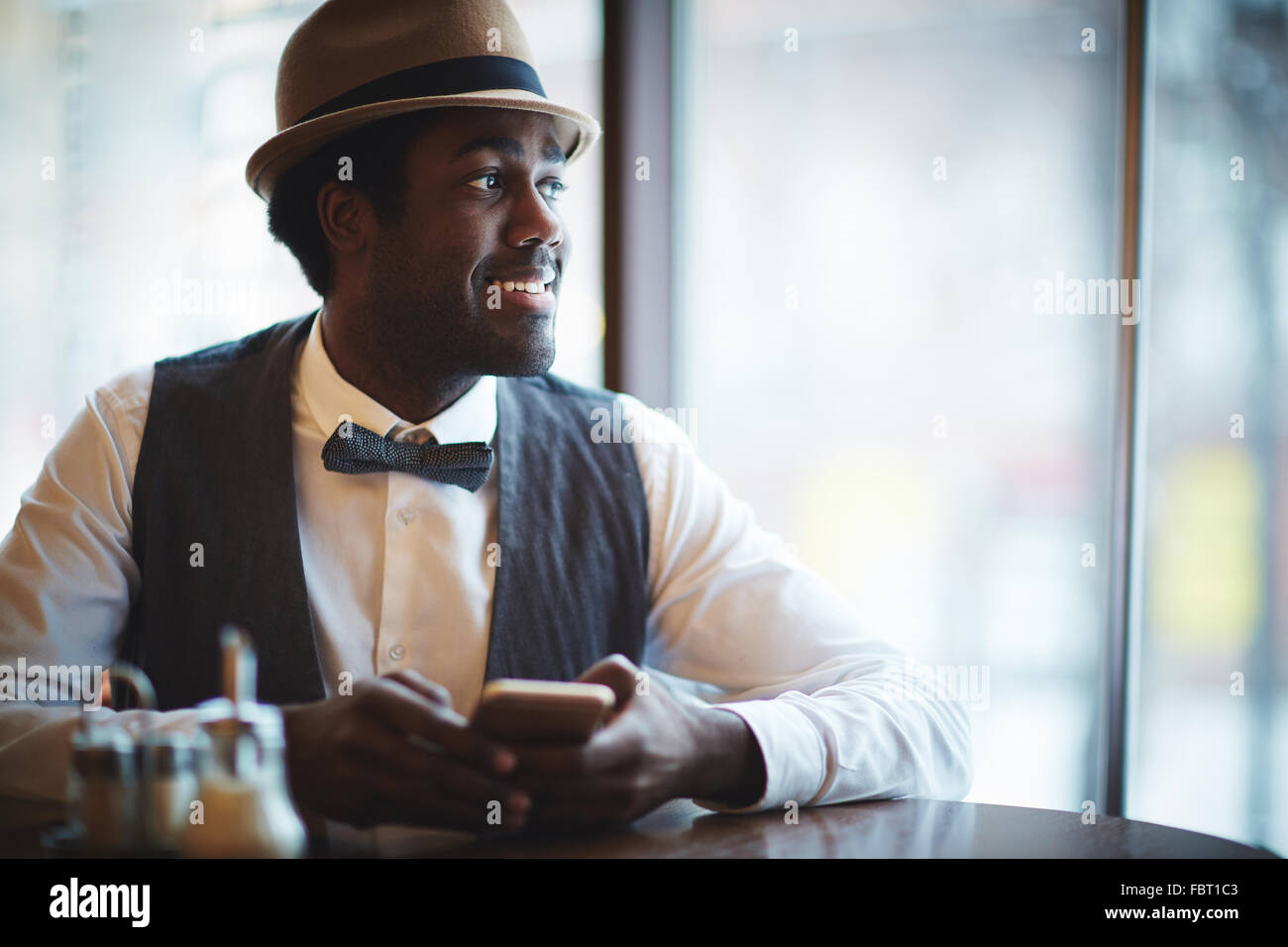 Eleganter junger Mann in Hut und intelligente Kleidung sitzen im café Stockfoto