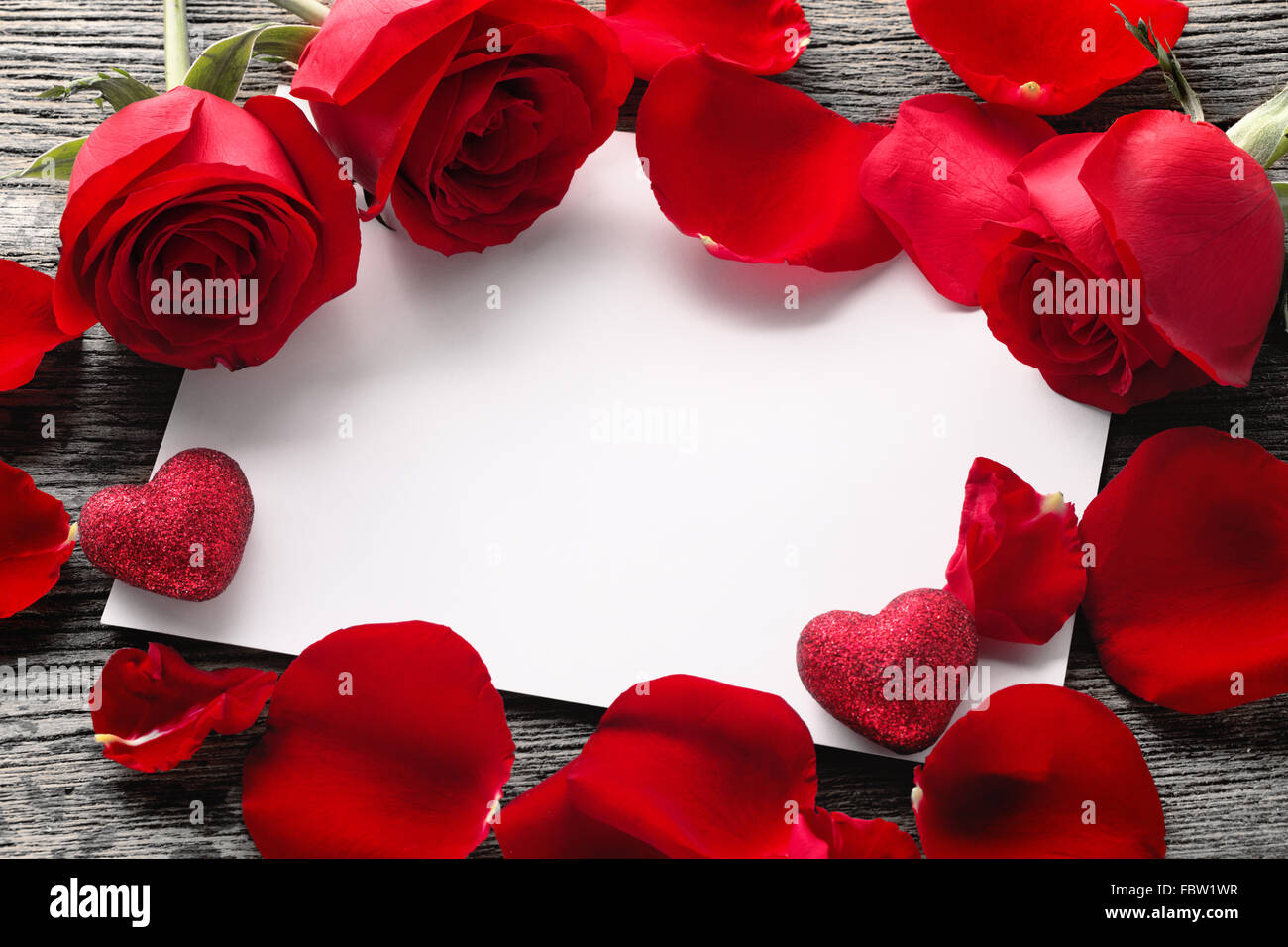 Valentinstag-Konzept: weiße leere Papierkarte, Rosen und Rosen Blütenblätter auf rustikalen hölzernen Hintergrund. Stockfoto