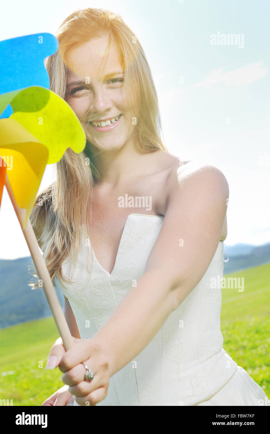 glückliche junge schöne Braut nach der Hochzeit Zeremonie Event haben Spaß im Freien auf der Wiese bei Sonnenuntergang mit Windmühle Spielzeug und Vertretung Stockfoto