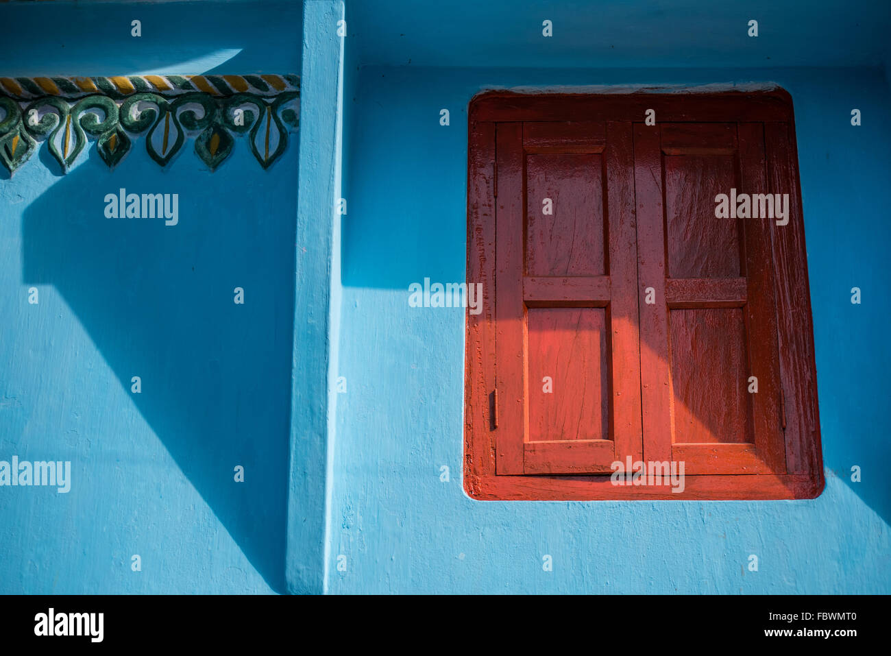 Eine kühne hellere blaue Wand mit indischen Relief und lebendige Orange shuttered Fenster.  Eine Studie von Linien, Schatten und Farbe färben. Stockfoto
