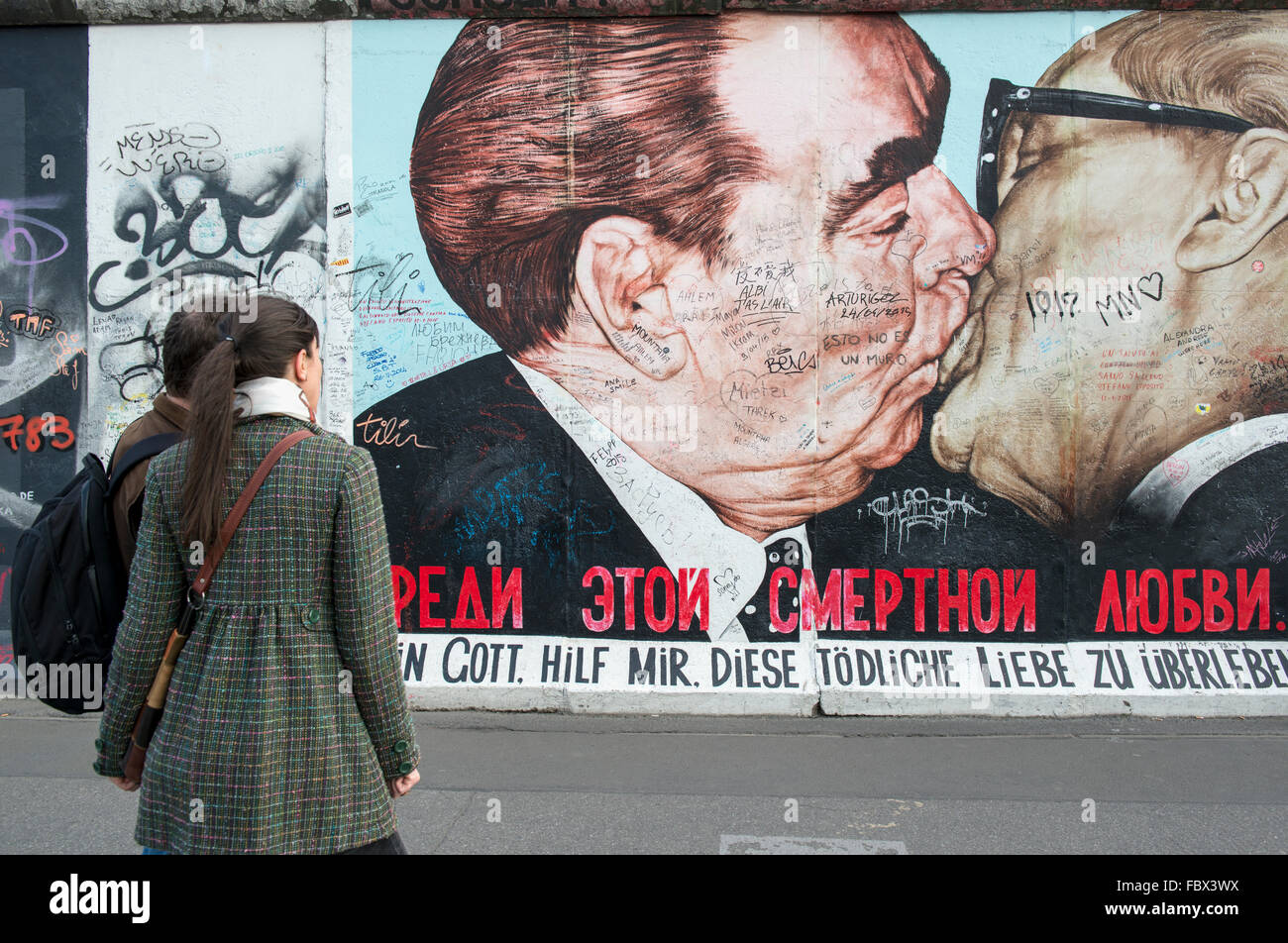 Touristen, die Anzeigen von Bildmaterial auf der Berliner Mauer an der East Side Gallery zeigt einen Kuss zwischen Leonid Brezhnev und Erich Honecker Stockfoto