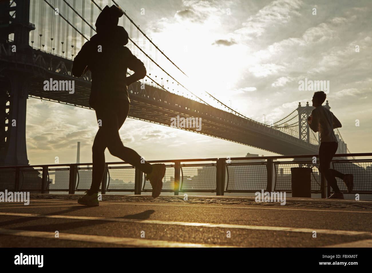 Sonnenaufgang über die Manhattan Bridge New York City morgen als zwei Jogger laufen North East River Esplanade Stockfoto