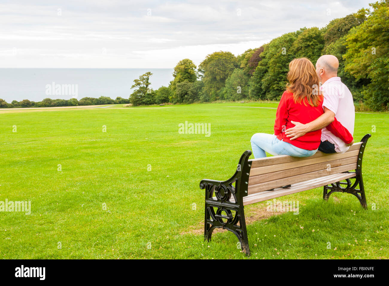 Rückansicht des mittleren Alters paar sitzt auf einer Bank mit Blick auf das Meer Stockfoto