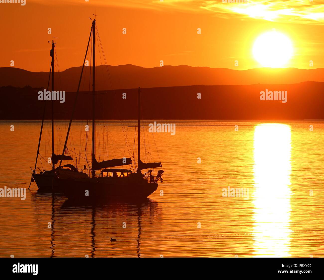 Ein Blick auf eine untergehende Sonne über einige festgemachten Sportboote in Fairlie Bucht, Ayrshire. Stockfoto