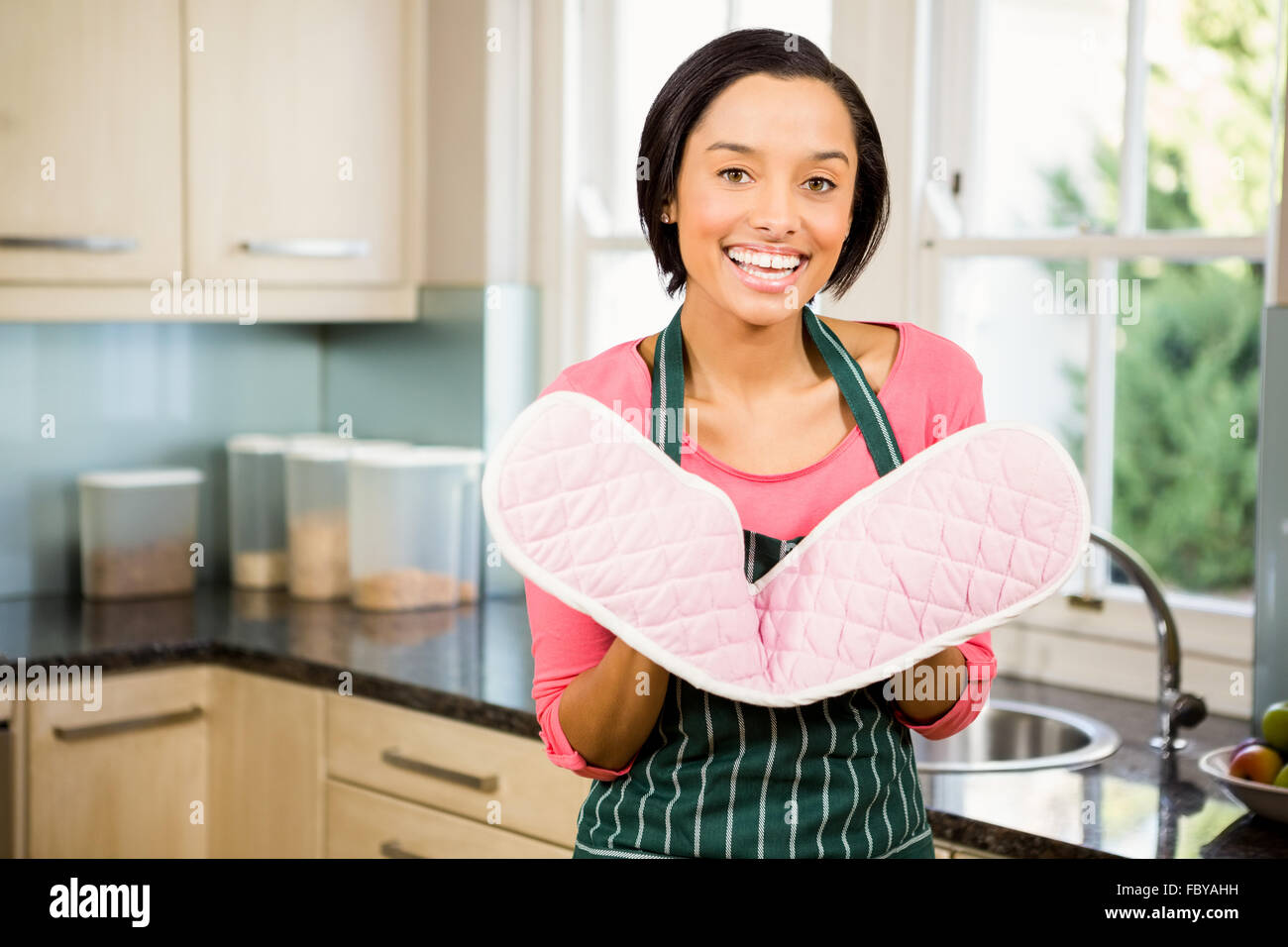 Lächelnde Brünette zeigt rosa Topfhandschuh Stockfoto