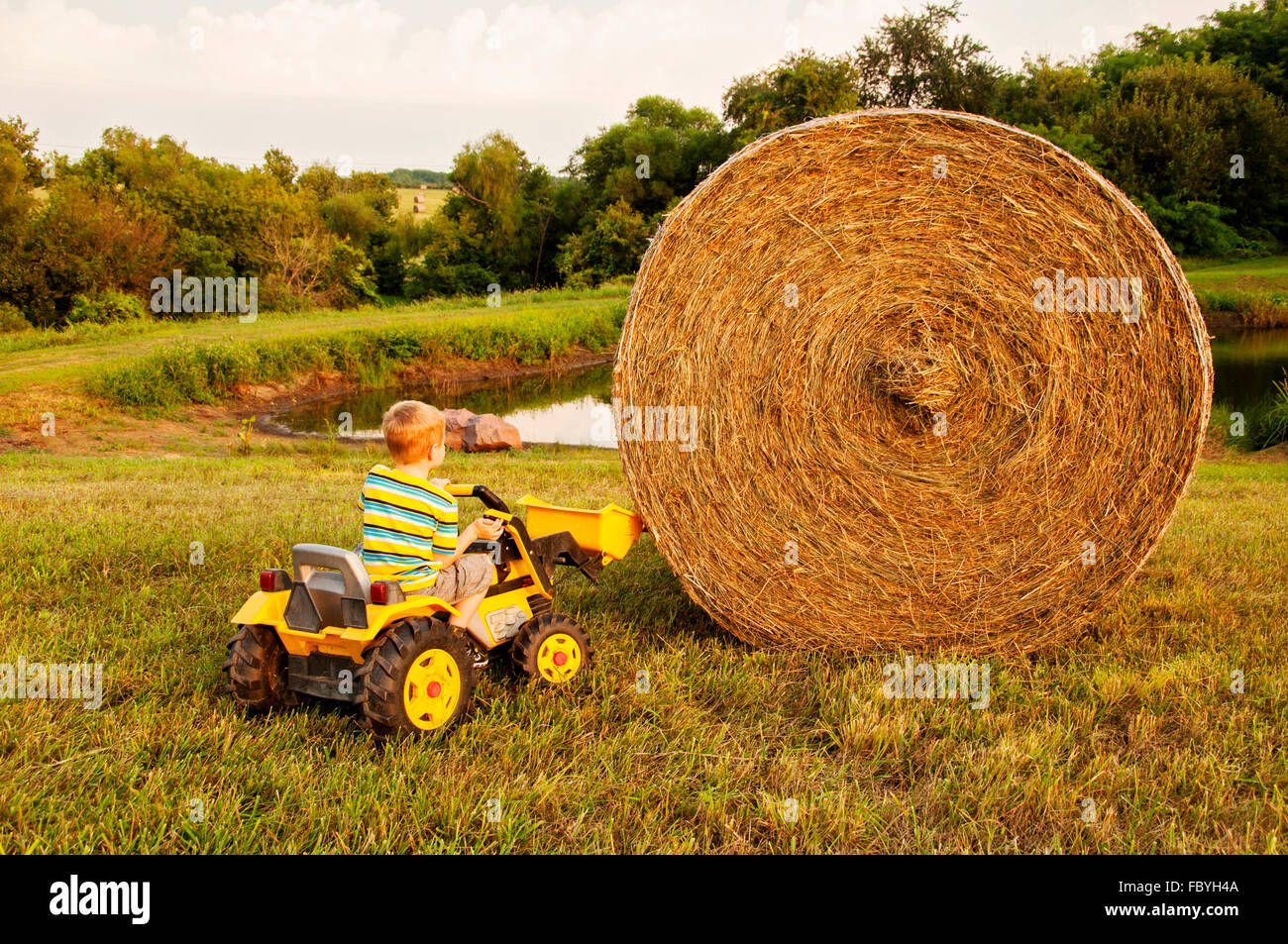 Junge versucht, heben Sie Haybale mit Eimer auf Spielzeug-Traktor Stockfoto