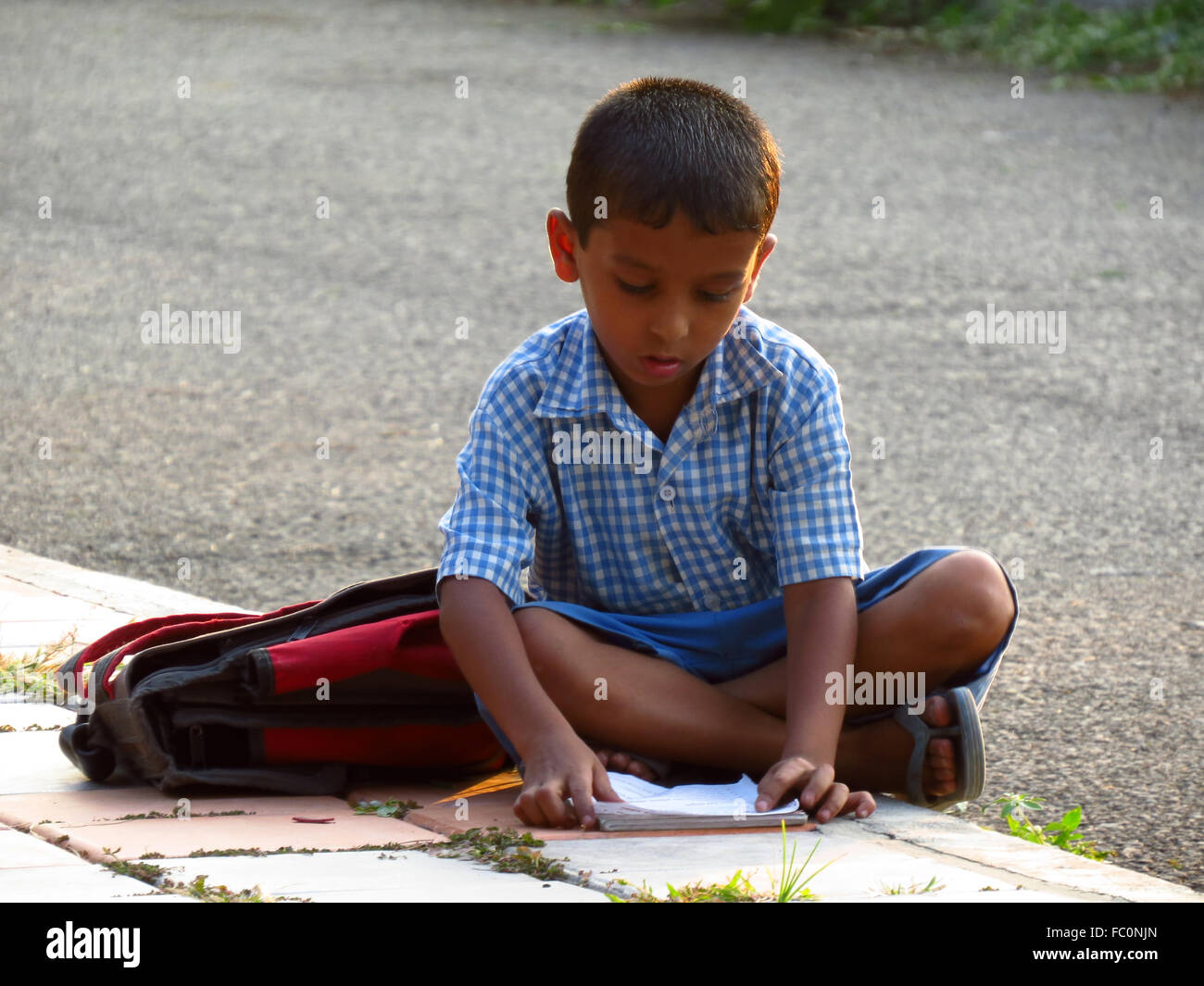 Ein kleinen indischen jungen setzt sich auf einen am Straßenrand Fußweg vor seiner Prüfung zu studieren. Stockfoto