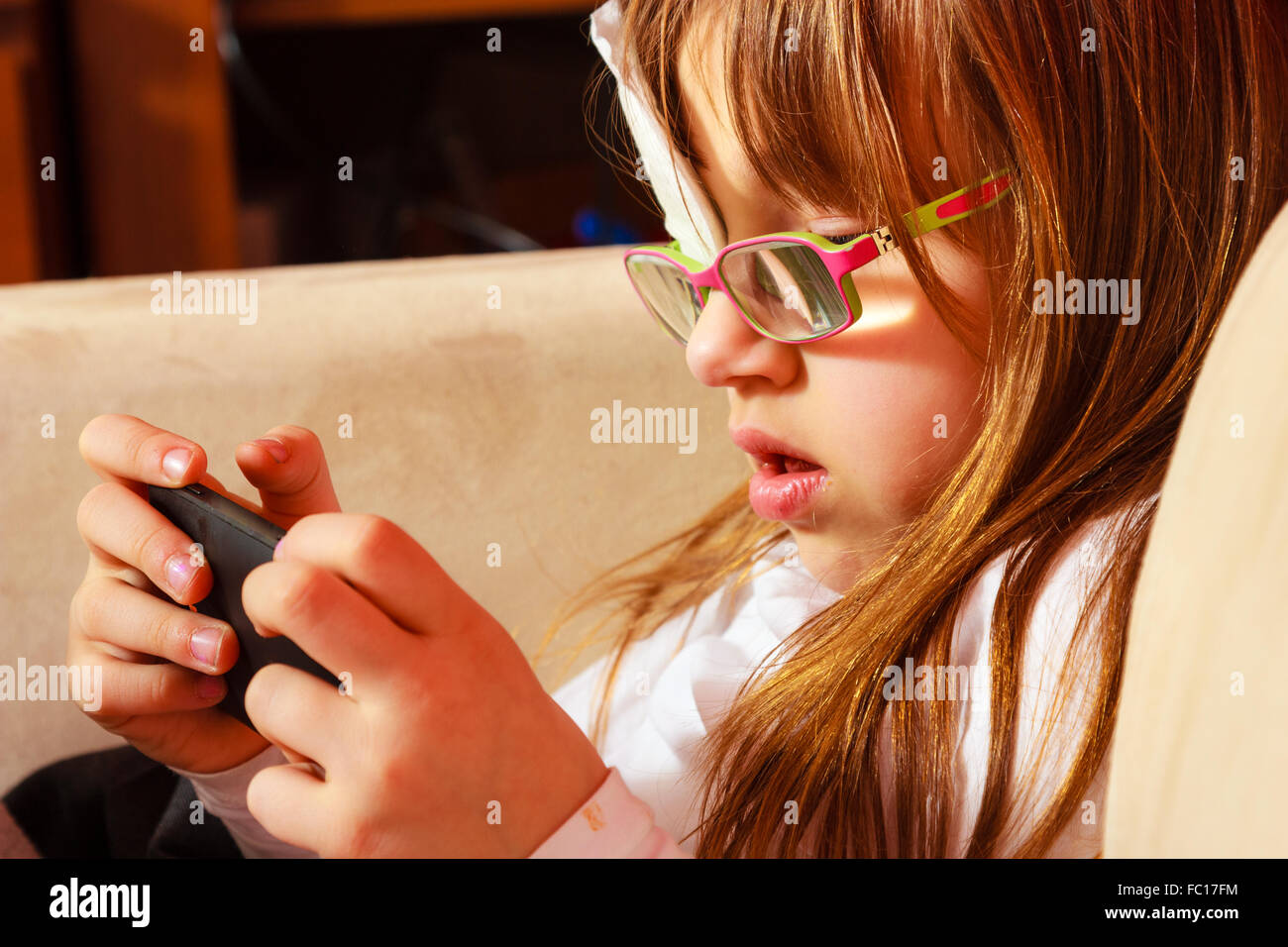 Mädchen in Gläsern auf Smartphone zu Hause spielen Stockfoto