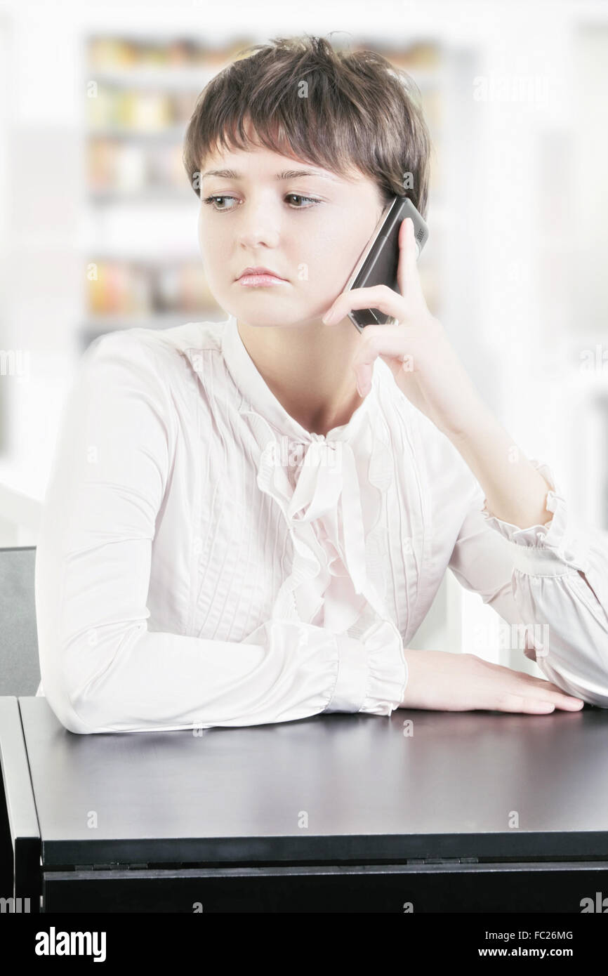 Junge Frau sitzt am Schreibtisch mit Telefon Stockfoto