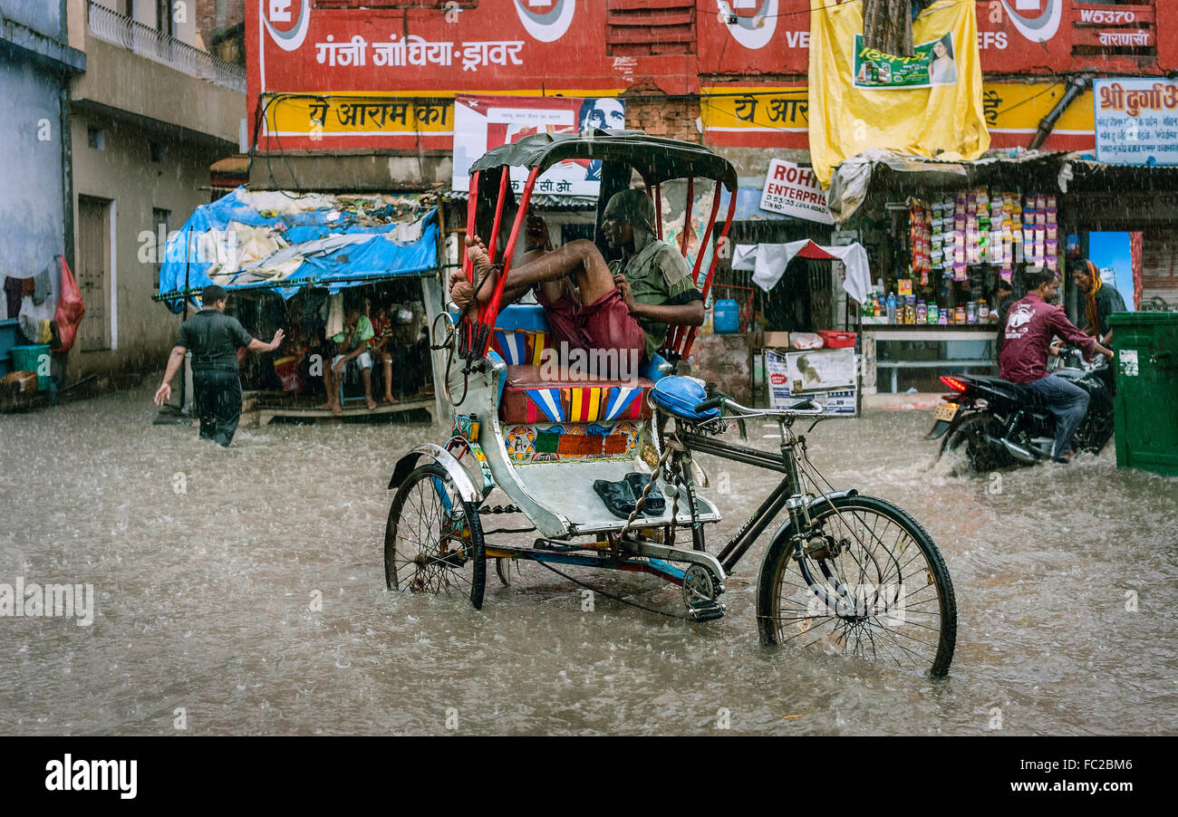 Mann sitzt im getauchten Fahrradrikscha, die noch auf der Suche Geschäft in schweren Flut und Regen. Stockfoto