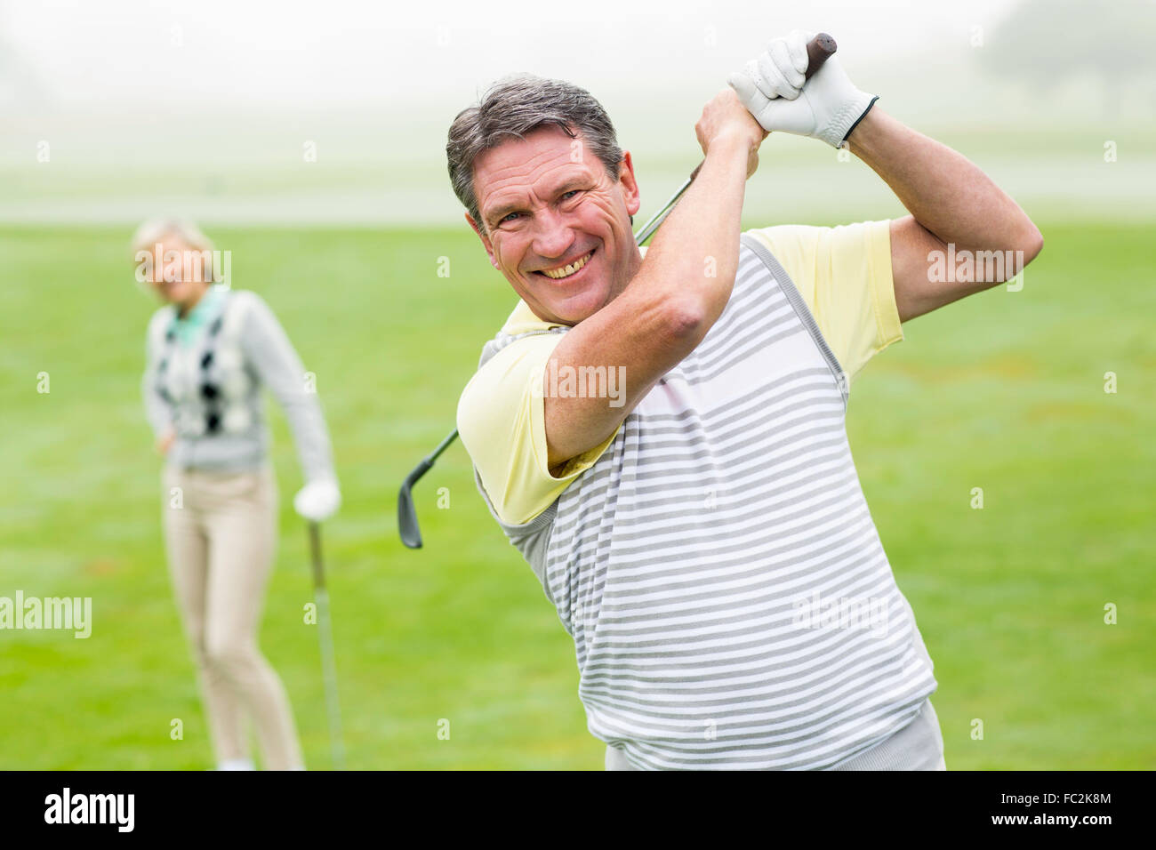 Glücklich Golfer mit Partner hinter ihm Abschlag Stockfoto