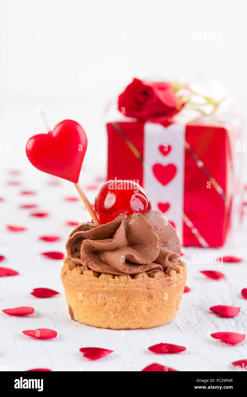 Schokolade Cupcake mit Kirsche vor Geschenkbox auf weißem Hintergrund aus Holz. Valentines Tag und Liebe Konzept. Stockfoto