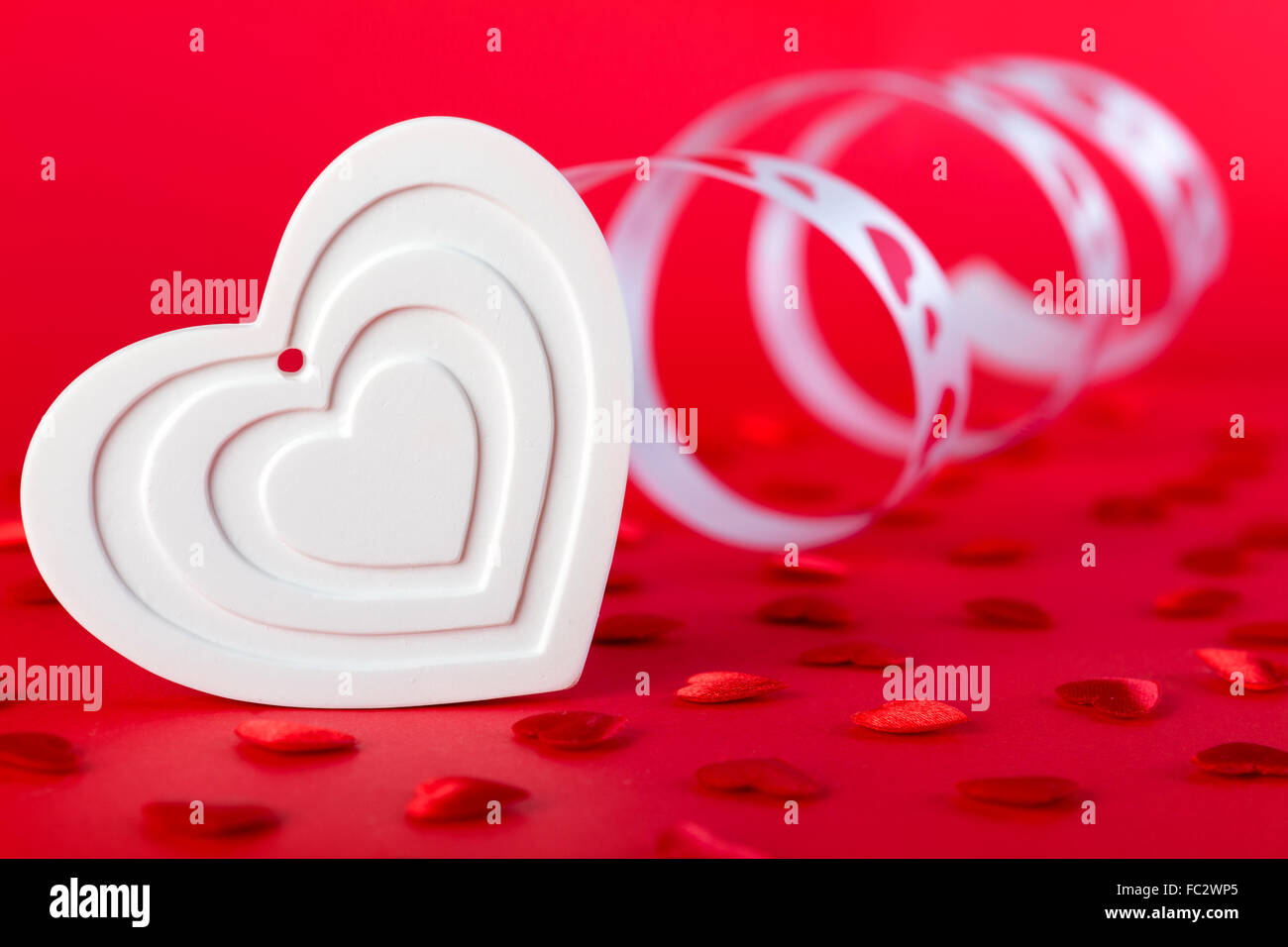 Weiße Form Herz mit Band und roten Herzen auf rotem Grund. Valentines Tag und Liebe Konzept. Stockfoto