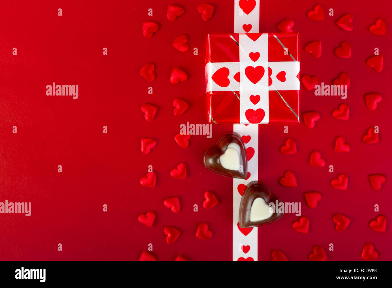 Geschenk mit weißen Band und Schokolade und roten Herz auf rotem Grund. Zum Valentinstag. Geschenk-Box im Mittelpunkt. Stockfoto