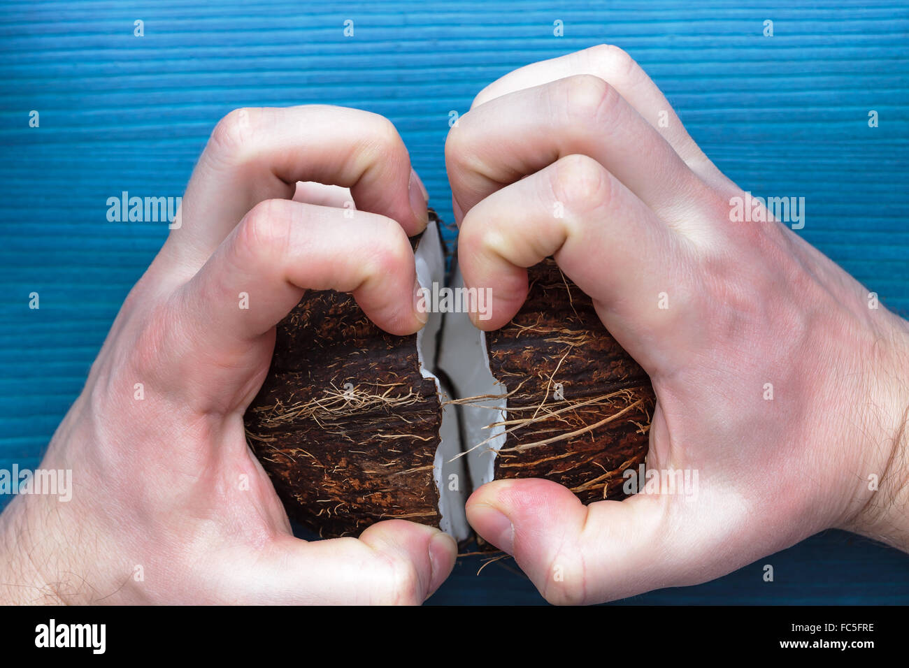 verärgerter Mann bricht eine Kokosnuss Walnuss in zwei Hälften Stockfoto