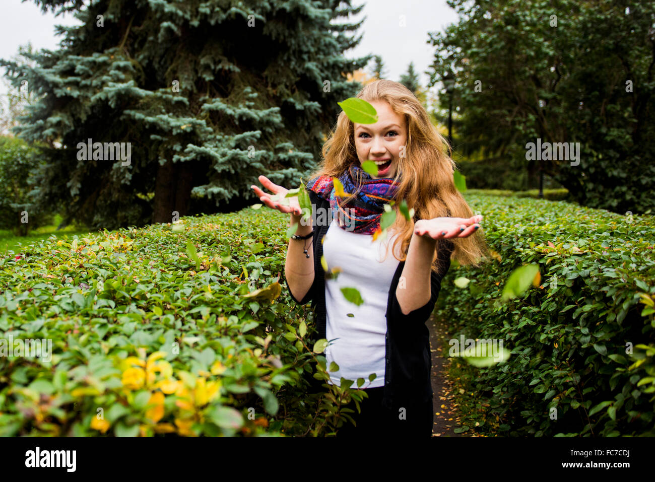 Kaukasische Frau wirft Blätter im Garten Stockfoto