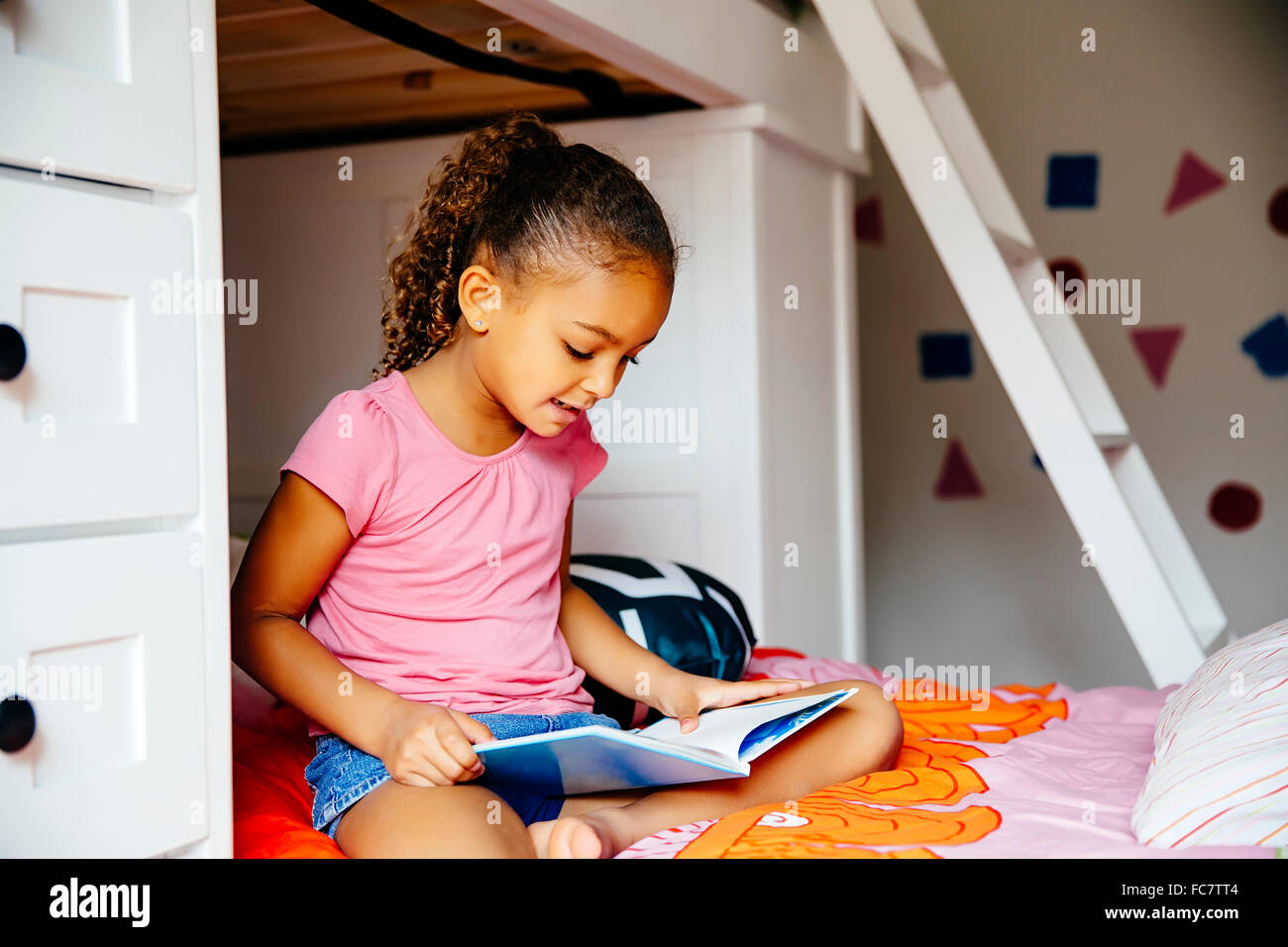 Gemischte Rassen Mädchen lesen auf Bett Stockfoto