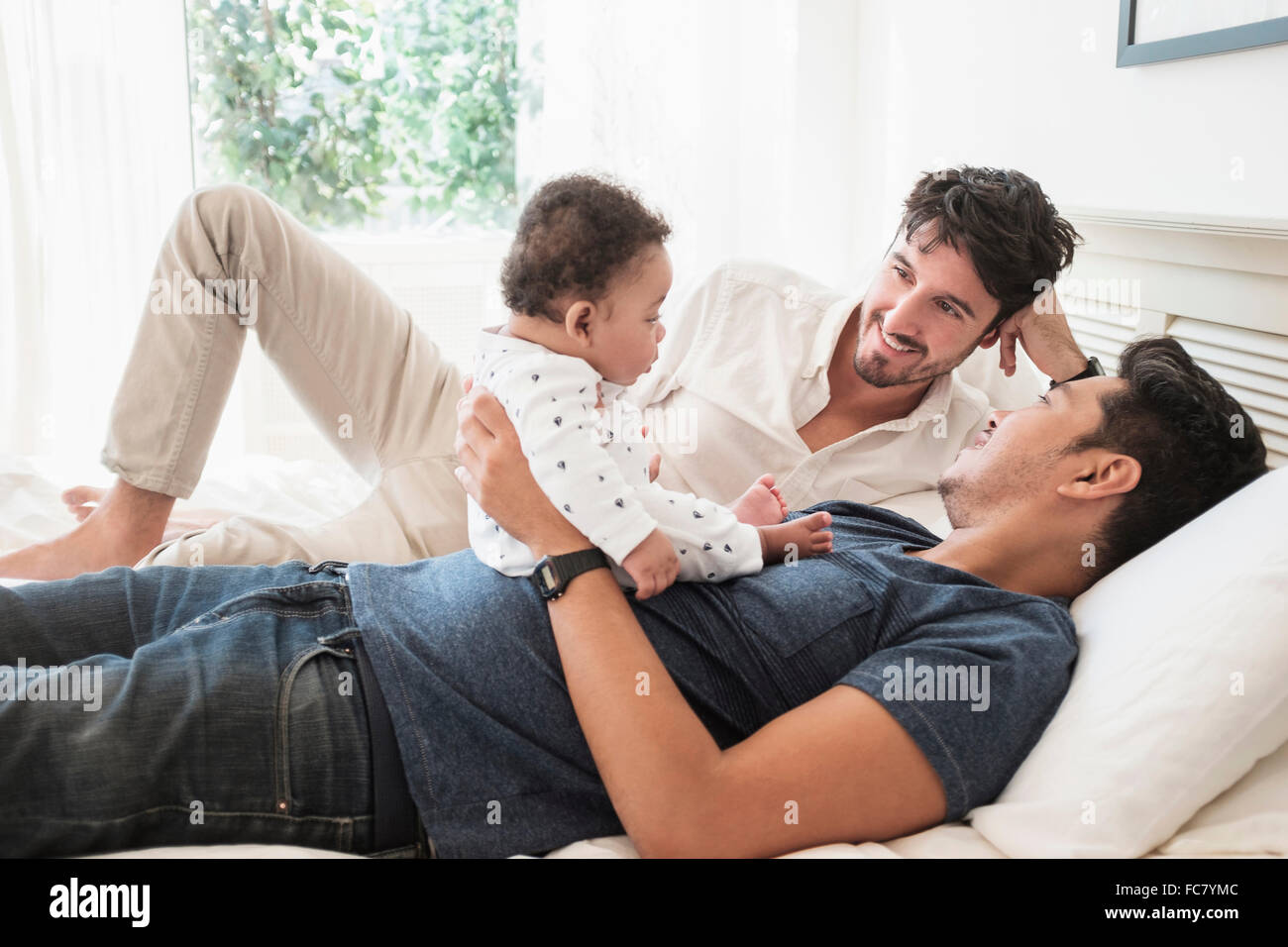 Schwule Väter spielen mit Baby Sohn auf Bett Stockfoto