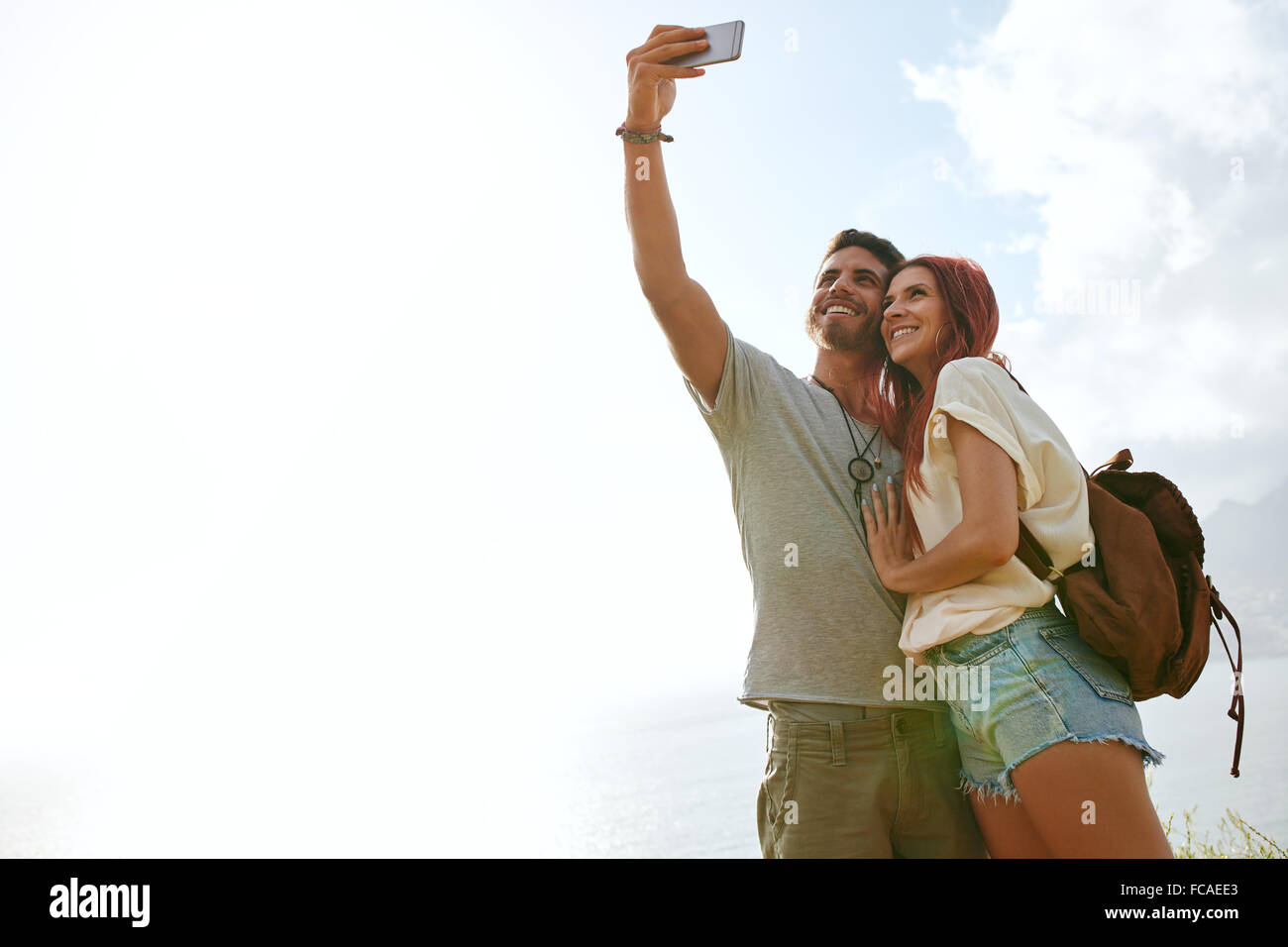 Niedrigen Winkel Blick auf jungen Liebespaar in den Sommerferien ein Selbstporträt mit Smartphone im freien nehmen. Entspannte junges Paar o Stockfoto