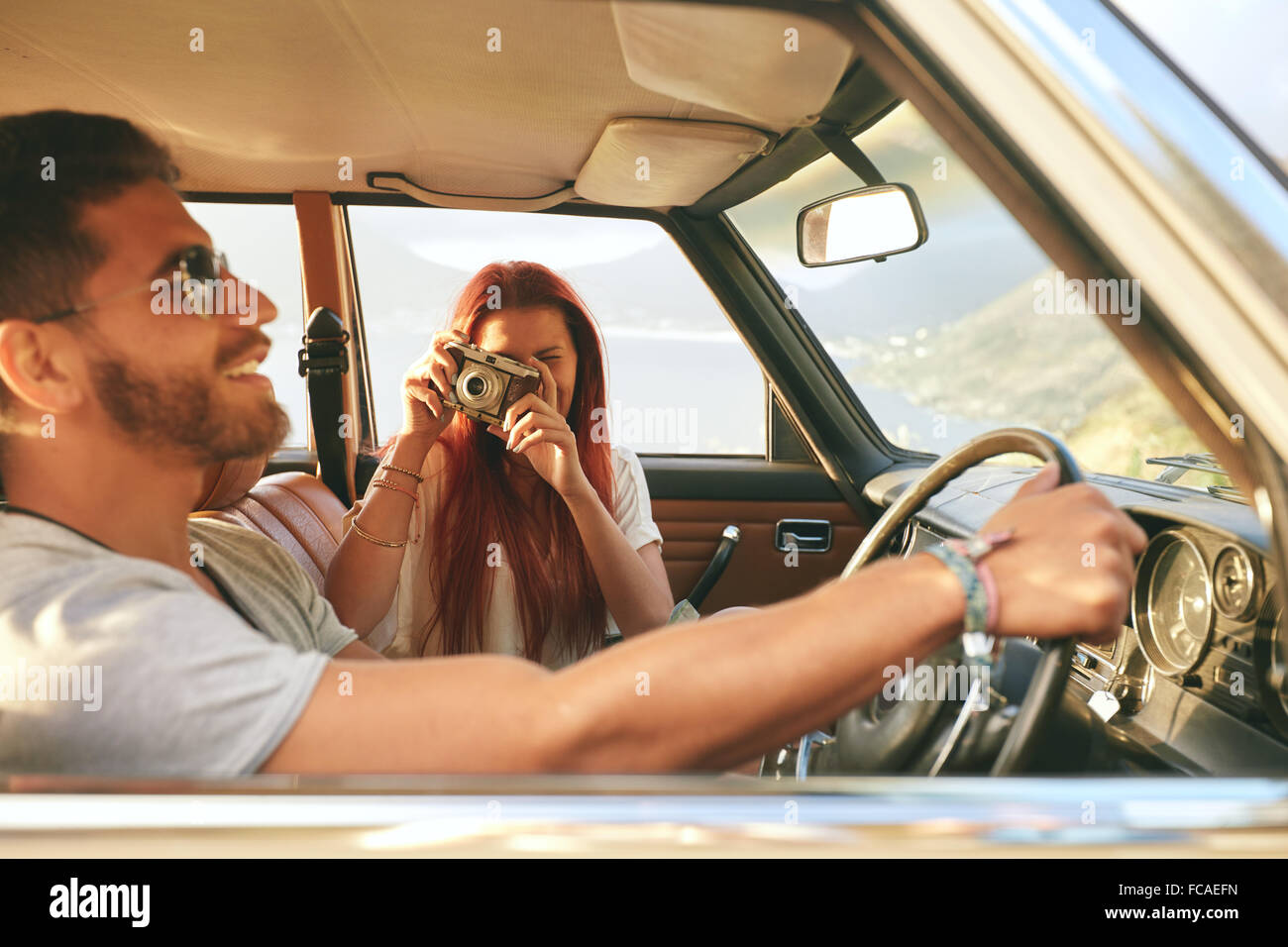 Junges Paar auf einem Roadtrip. Steuerwagen mit Frau fotografieren mit Retro-Kamera Mann. Stockfoto