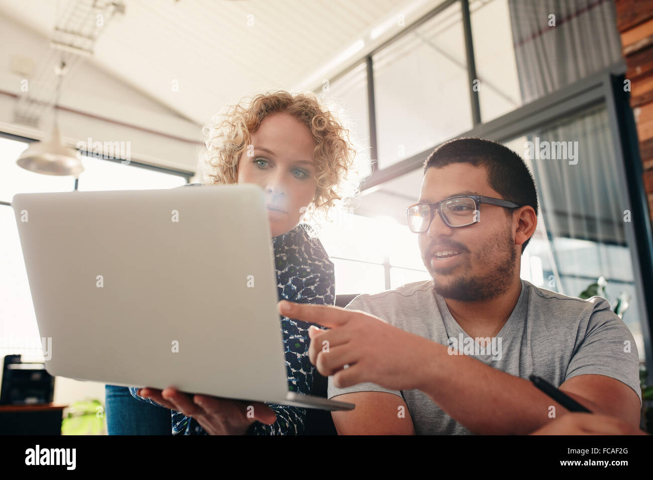 Zwei junge Grafik-Designer arbeiten in ihrem eigenen Büro. Mann zeigte am Laptop in Frauenhand. Stockfoto