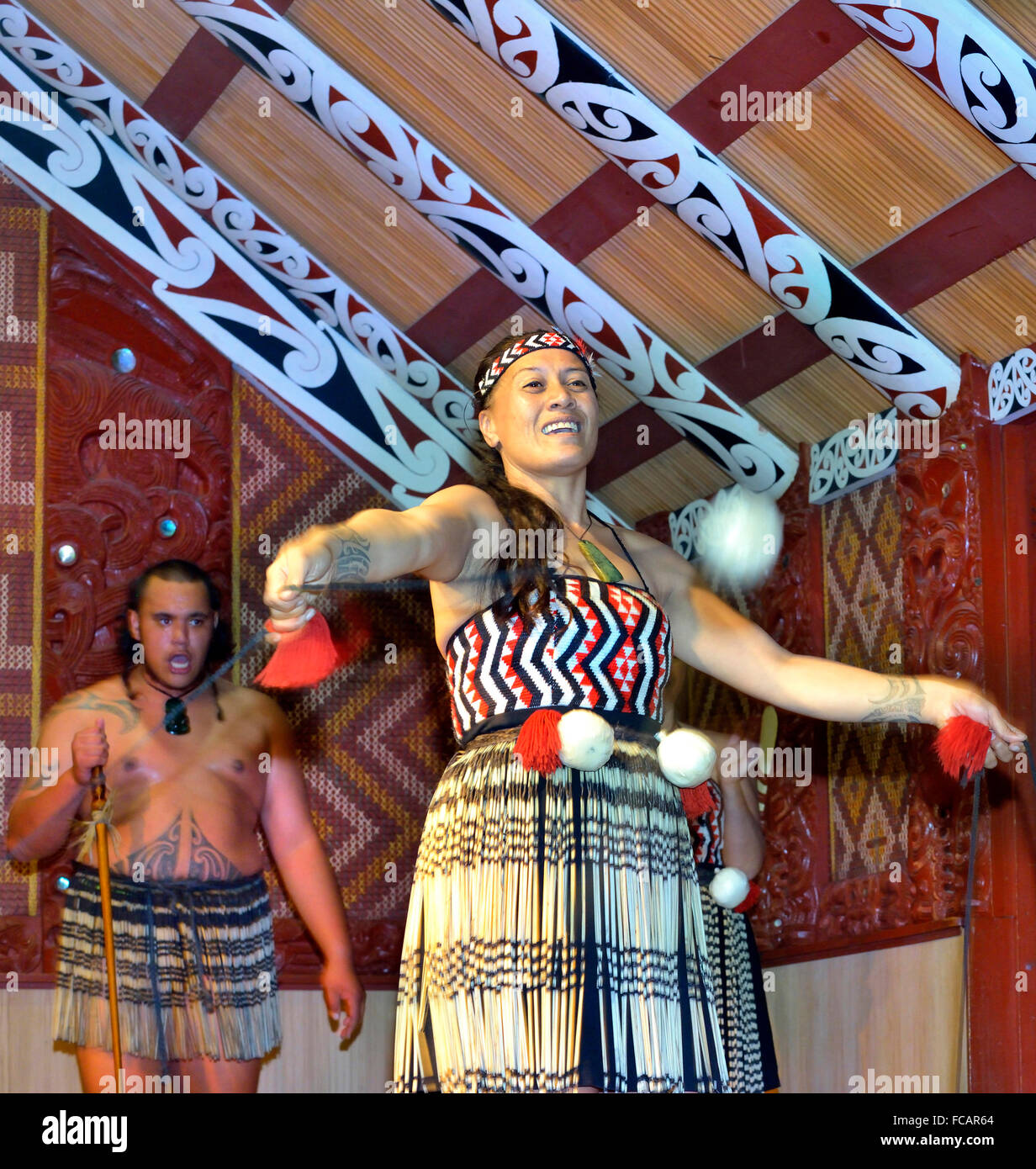 Maori-Frau und Maori-Mann in Te Puia, Rotorua. Frau tanzt mit POI(s), während der Mann im Versammlungshaus, Nordinsel, Neuseeland, singt Stockfoto