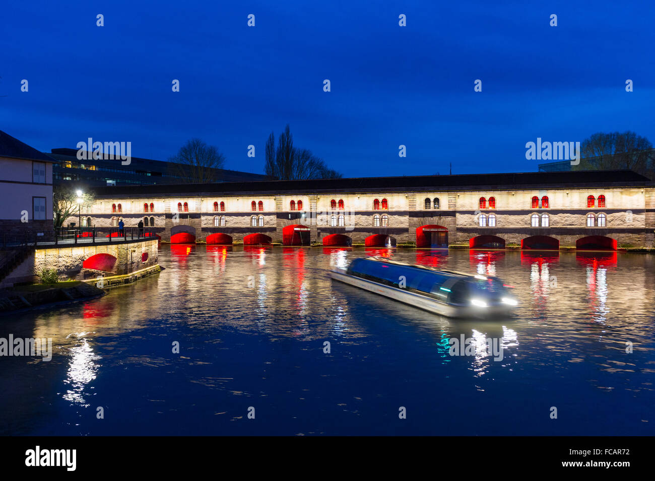 Ausflugsschiff mit Touristen vor der Barrage Vauban (Vauban-Wehr) nachts entlang dem Fluss Ill, Straßburg, Frankreich Stockfoto