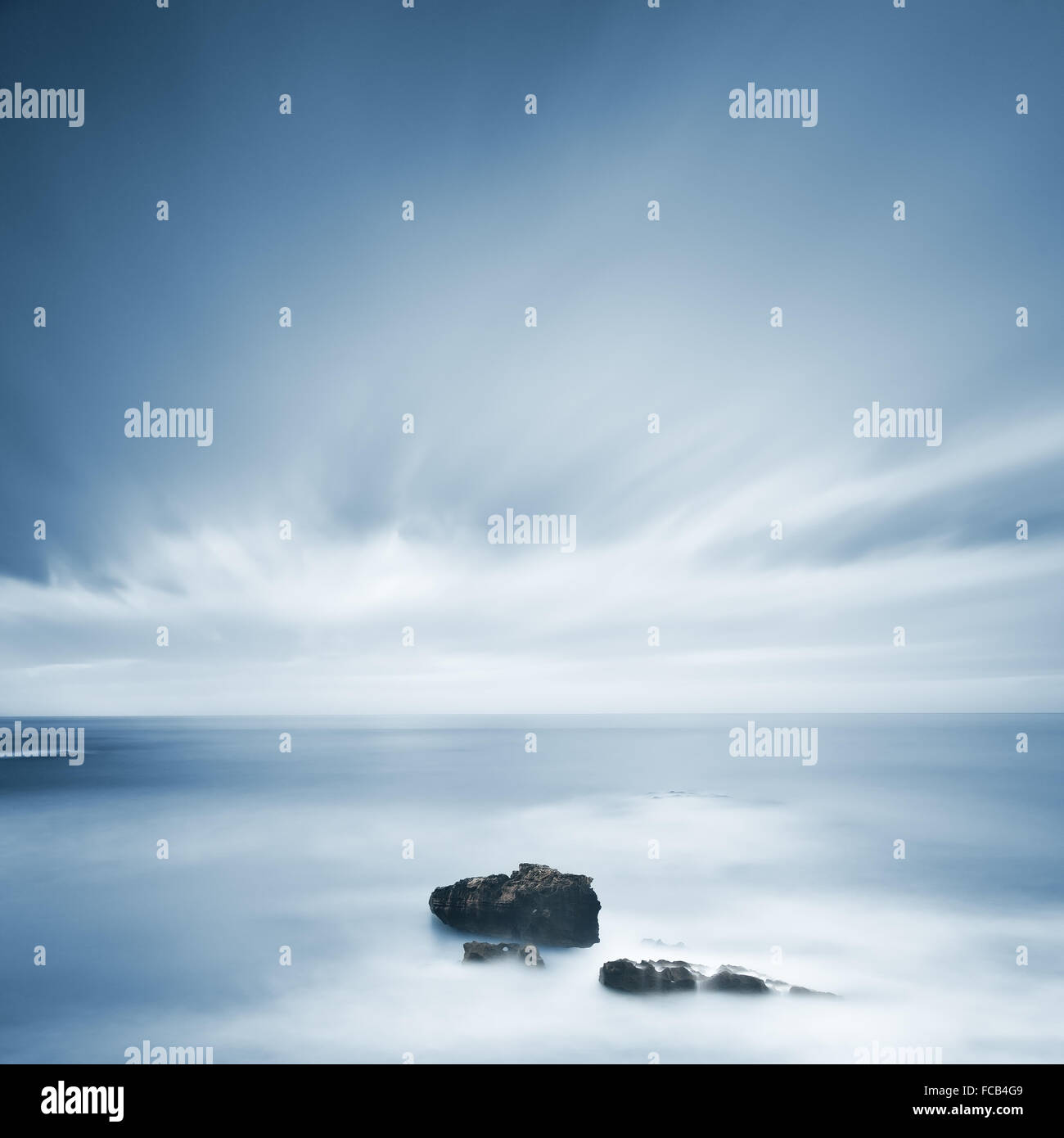 Dunklen Felsen in einem blauen Ozean unter bewölktem Himmel bei schlechtem Wetter. Langzeitbelichtung Fotografie Stockfoto