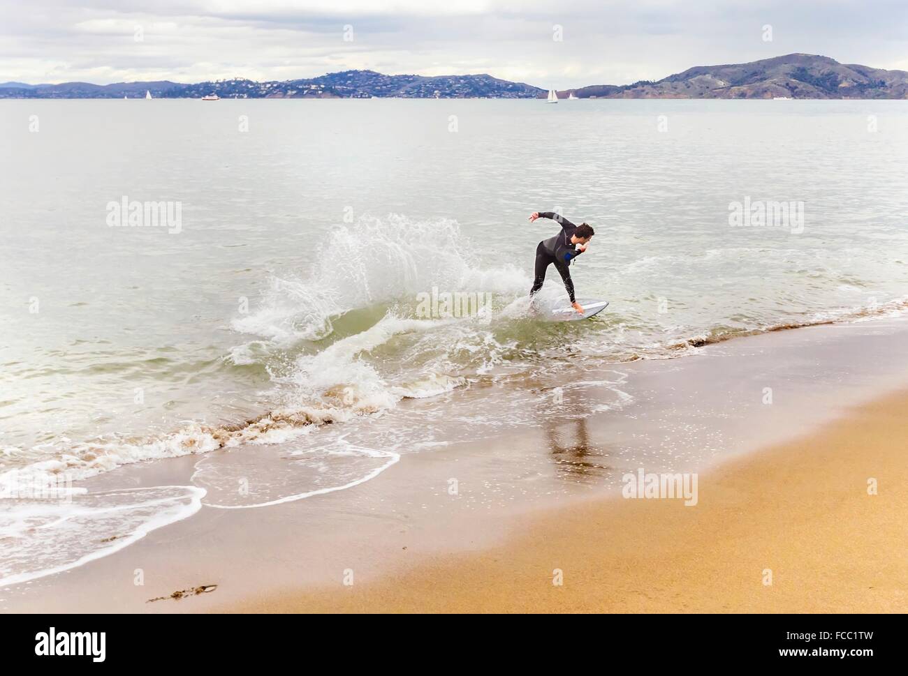 Blick auf ein Surfer im Neoprenanzug Surfen sein Board oder Skimboarding im seichten Wasser in der Bucht von San Francisco, an der Strandküste, sa Stockfoto