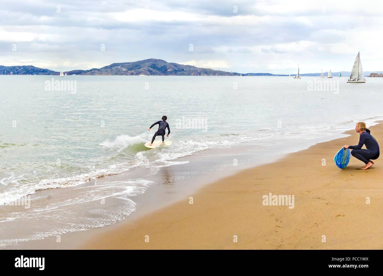 Blick auf ein Surfer im Neoprenanzug Surfen sein Board oder Skimboarding im seichten Wasser in der Bucht von San Francisco, an der Strandküste, sa Stockfoto