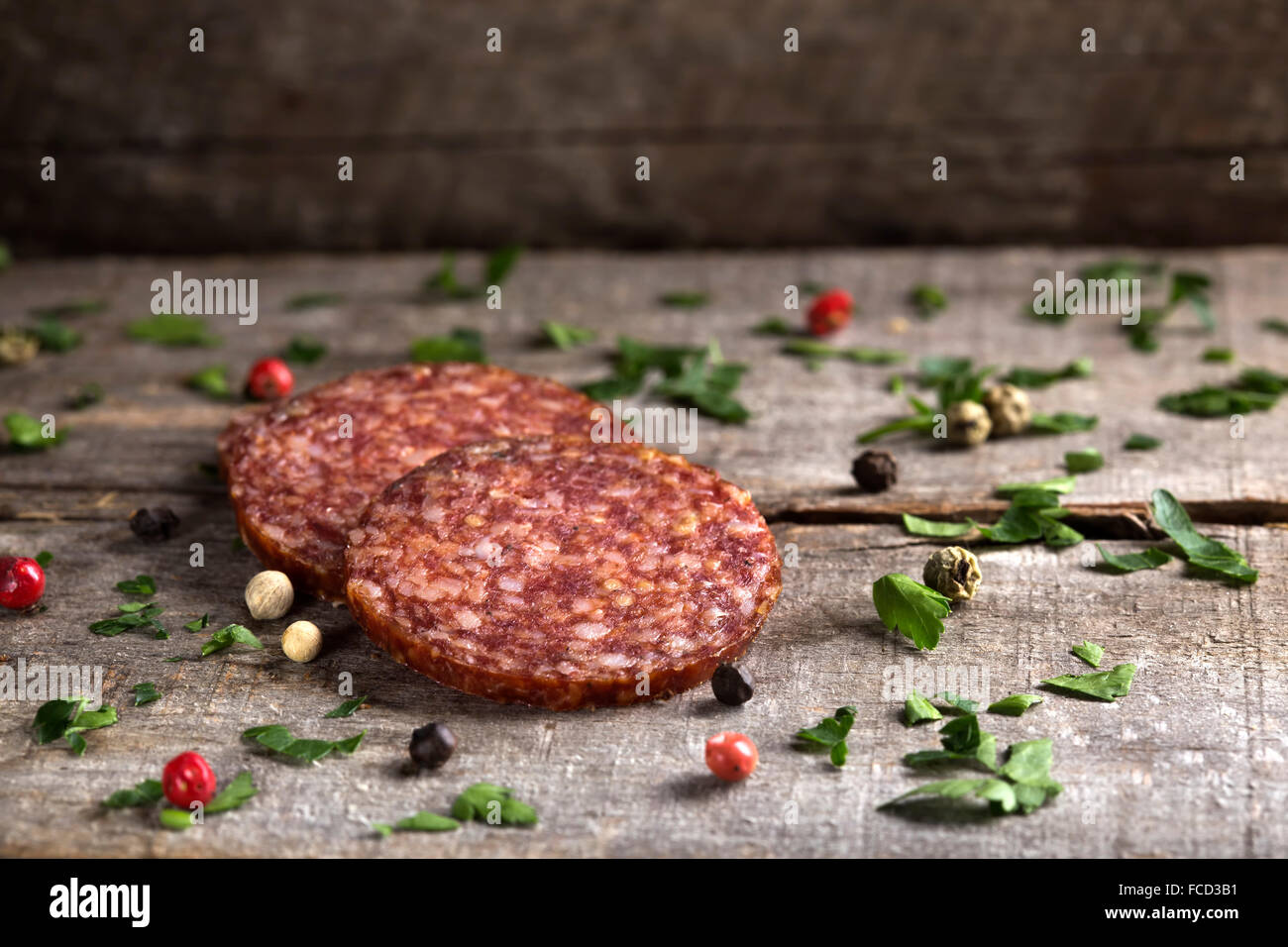Salami-Scheiben mit Petersilie und Pfeffer über hölzerne Hintergrund Stockfoto