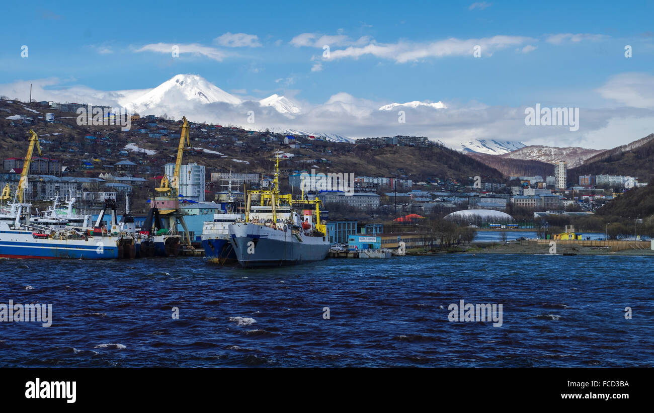 Hafen von Petropavlovsk-Kamchatskiy, Kamtschatka, Russland, gesehen von der Awatscha-Bucht. Gebäude und verschneite Koryaksky Vulkan im Hintergrund. Stockfoto