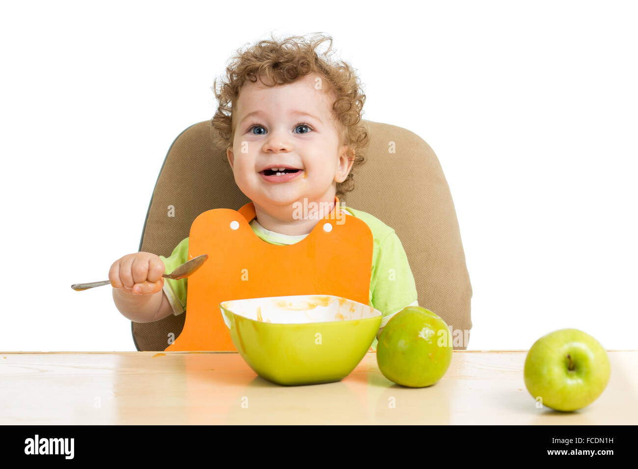 kleines Kind isst mit Löffel sitzen am Tisch mit Früchten Stockfoto