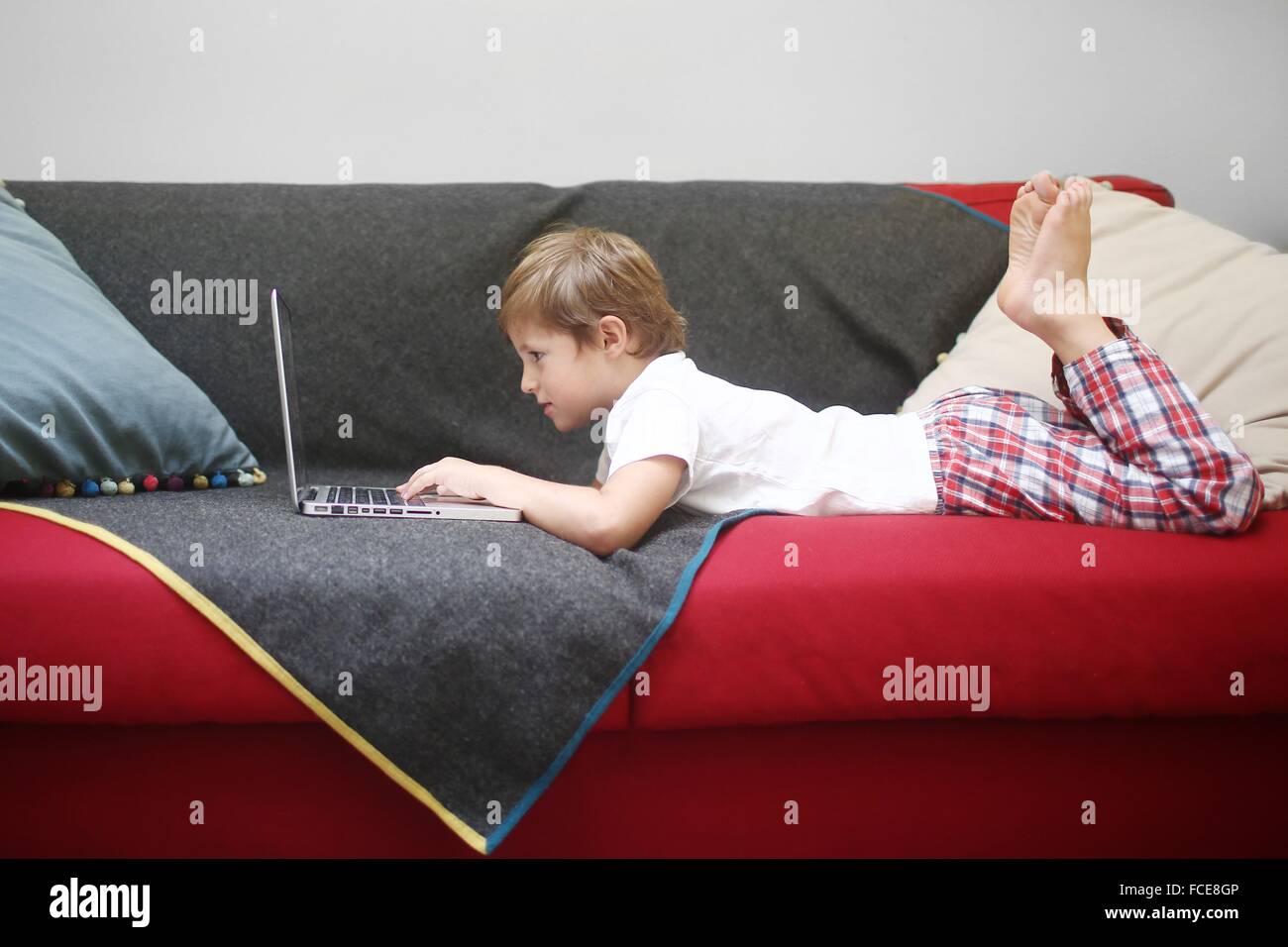 5 Jahre alter Junge Blick auf einem Computer, auf einem Sofa liegend Stockfoto