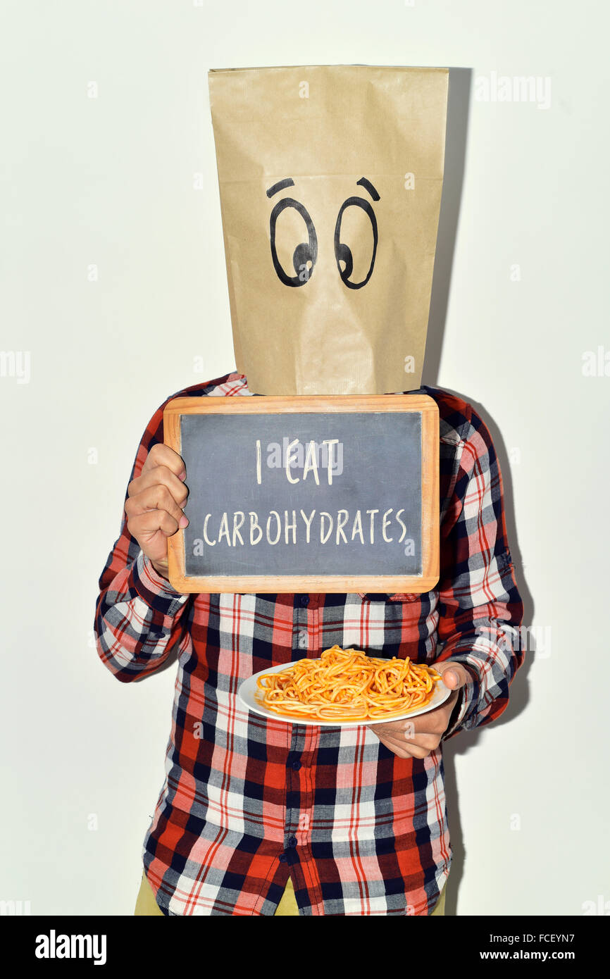 ein junger kaukasischer Mann mit einer Papiertüte in seinem Kopf mit lustigem Gesicht zeigt einer Tafel mit dem Text ich esse Kohlenhydrate und eine Stockfoto