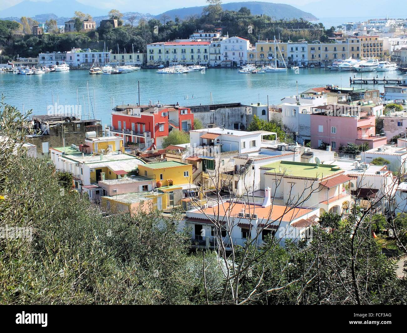 Mit Blick auf den Hafen von Ischia Porto auf tiefstehende Sonne. Die dunkle Farbe des Meeres macht einen schönen Kontrast mit dem helleren Blau des Himmels. Im Hintergrund die Insel Procida und den Vesuv. Stockfoto