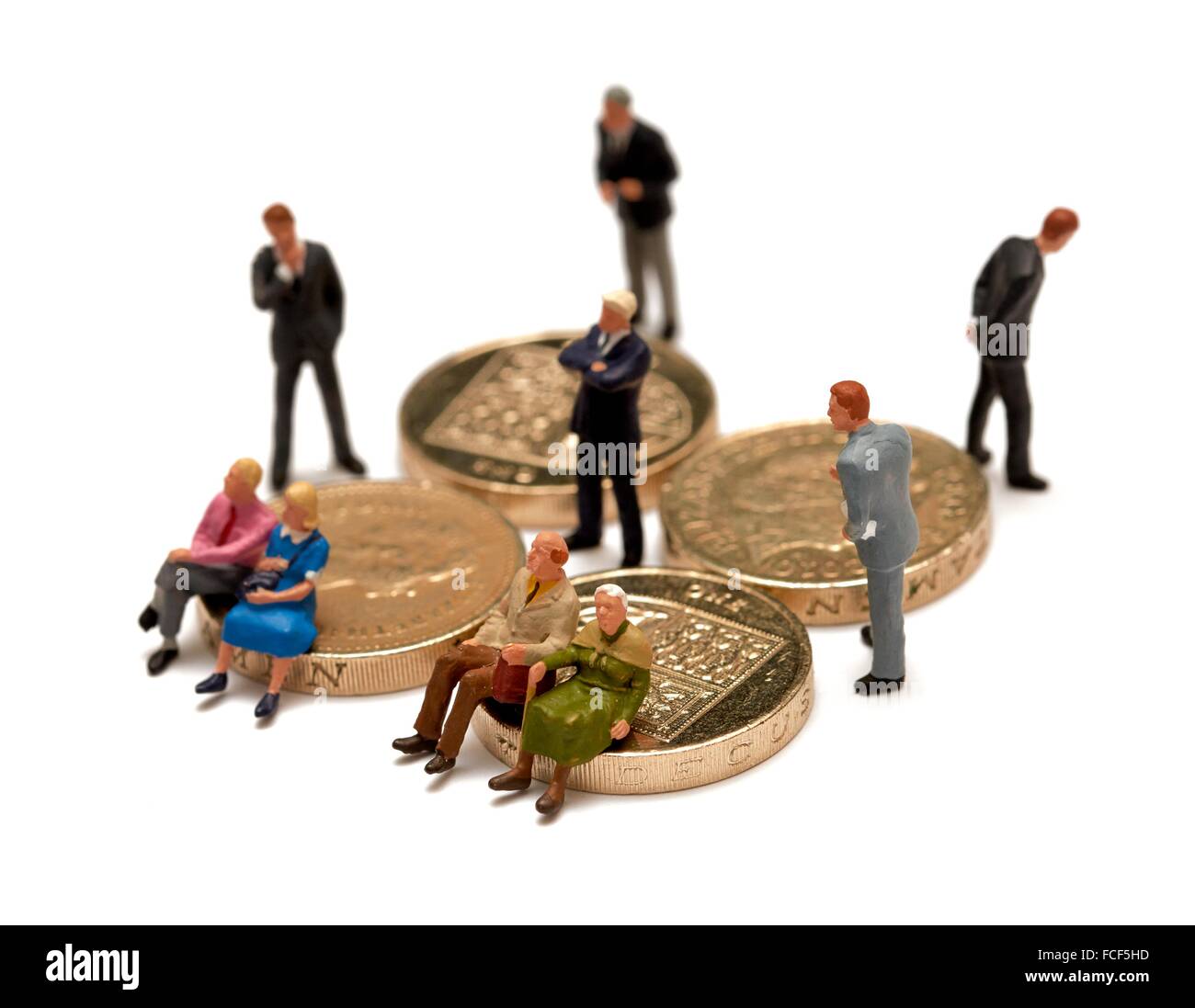 2 Miniatur-Paare sitzen auf britischen Münzen umgeben von Finanzberater in Anzügen Konzept. Stockfoto