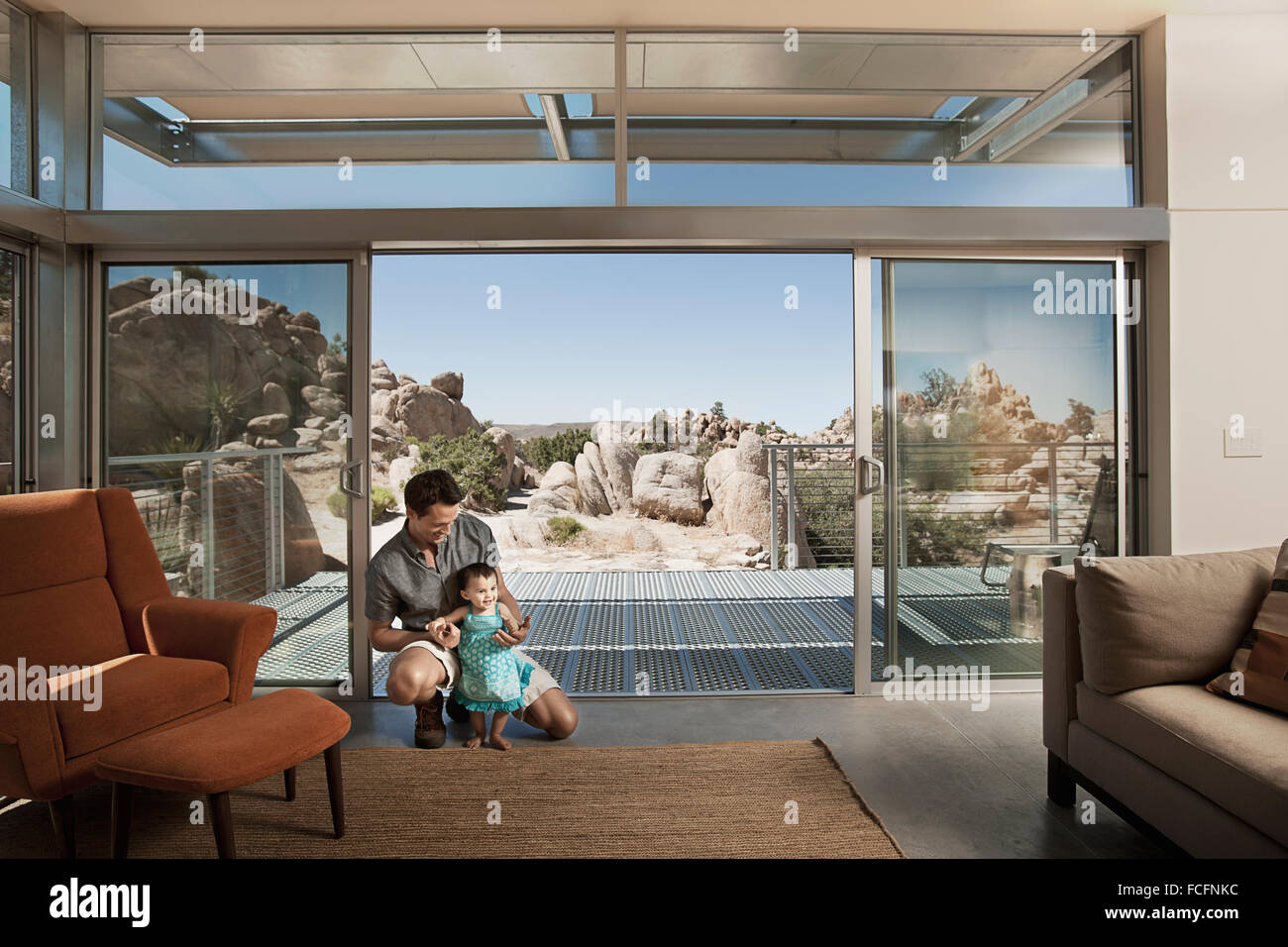 Ein Mann und ein kleines Kind in ein Ökohaus, ein Haus mit großen Glaswänden und Blick über die felsige Landschaft. Stockfoto
