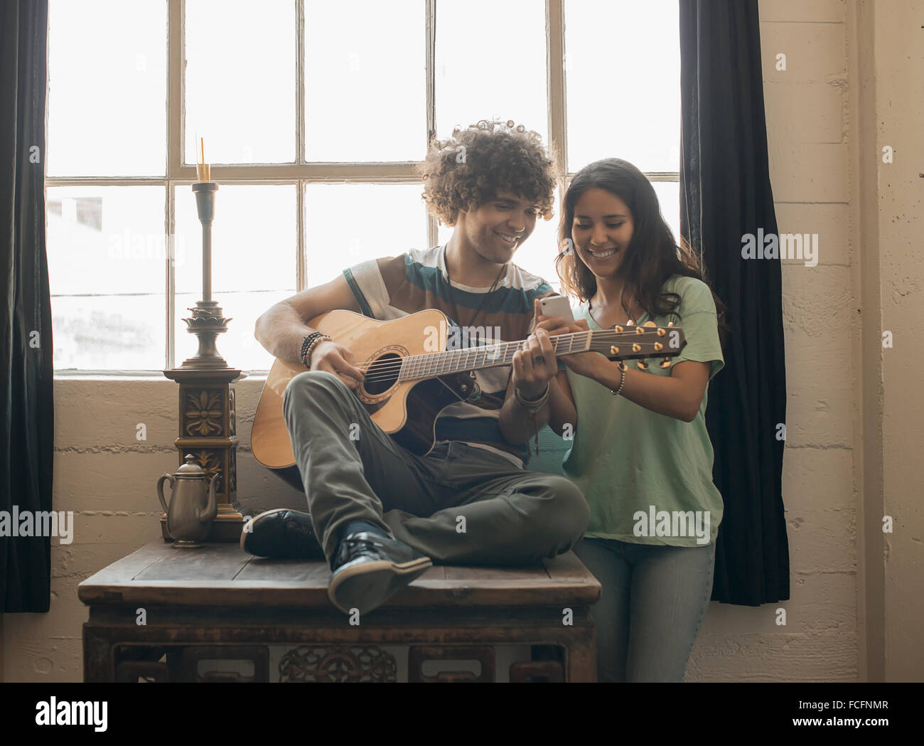 Loft-lebendigen. Ein junger Mann spielt Gitarre und eine Frau neben ihm fotografieren mit einem smart-Phone. Stockfoto