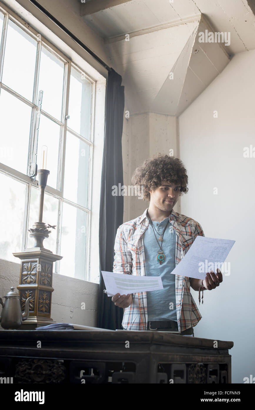 Loft-lebendigen. Ein junger Mann durch eine Tabelle mit Papierkram. Stockfoto