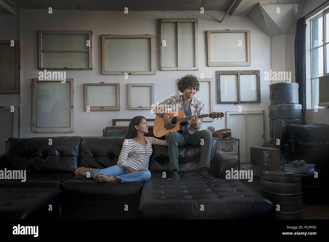 Loft-Wand mit Bilderrahmen, ein Mann, eine Gitarre und eine Frau auf einem Sofa sitzt. Stockfoto