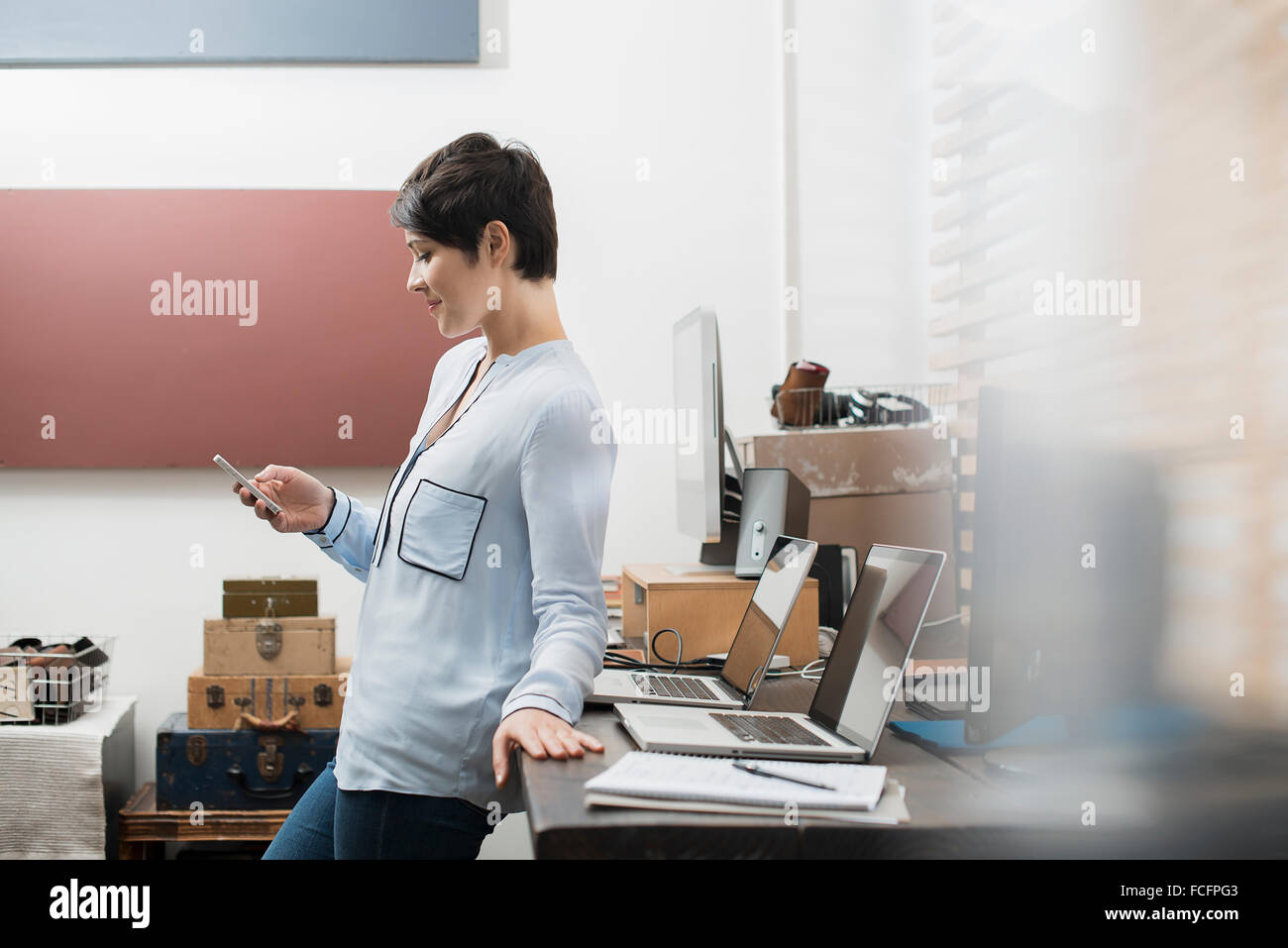 Eine Frau in einem Heimbüro mit einem Schreibtisch mit zwei Laptops, überprüfen ihr Smartphone. Stockfoto