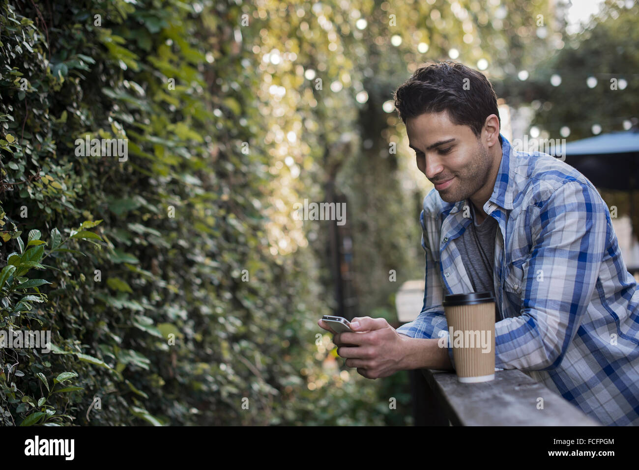 Ein Mann sitzt an einem Cafétisch im Freien, mit seinem Handy. Stockfoto