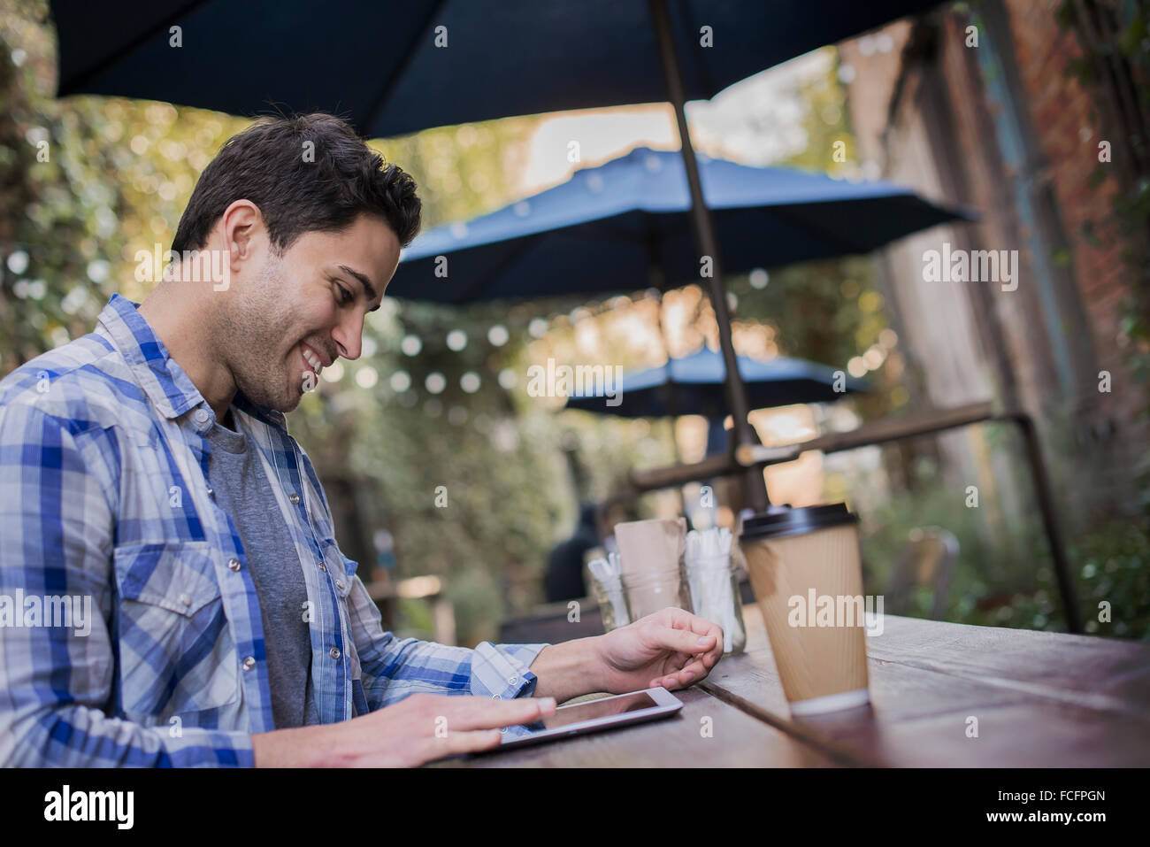 Ein Mann sitzt an einem Cafétisch im Freien, mit seinem Handy. Stockfoto