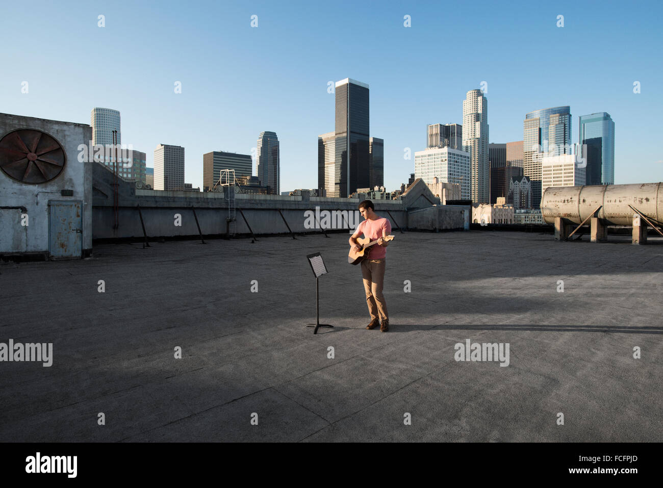 Ein Mann steht auf einer Dachterrasse mit Blick auf die Stadt, eine Gitarre zu spielen. Stockfoto