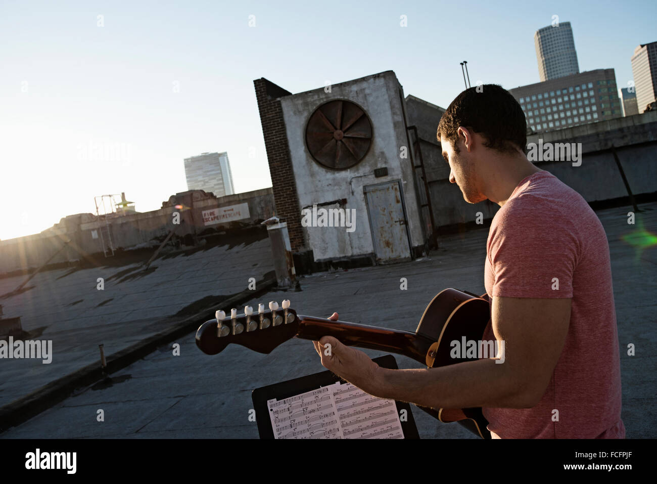 Ein Mann, eine Gitarre, Sititng auf der Dachterrasse mit Blick auf die Stadt in der Dämmerung. Stockfoto