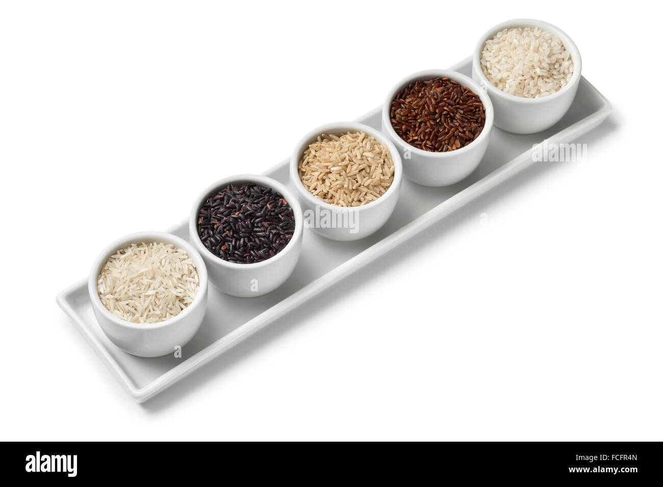 Schalen mit verschiedenen Arten von roher Reis auf weißem Hintergrund Stockfoto