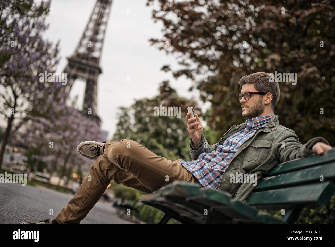Ein Mann sitzt auf einer Parkbank in der Champs de Mars unter dem Eiffelturm. Stockfoto