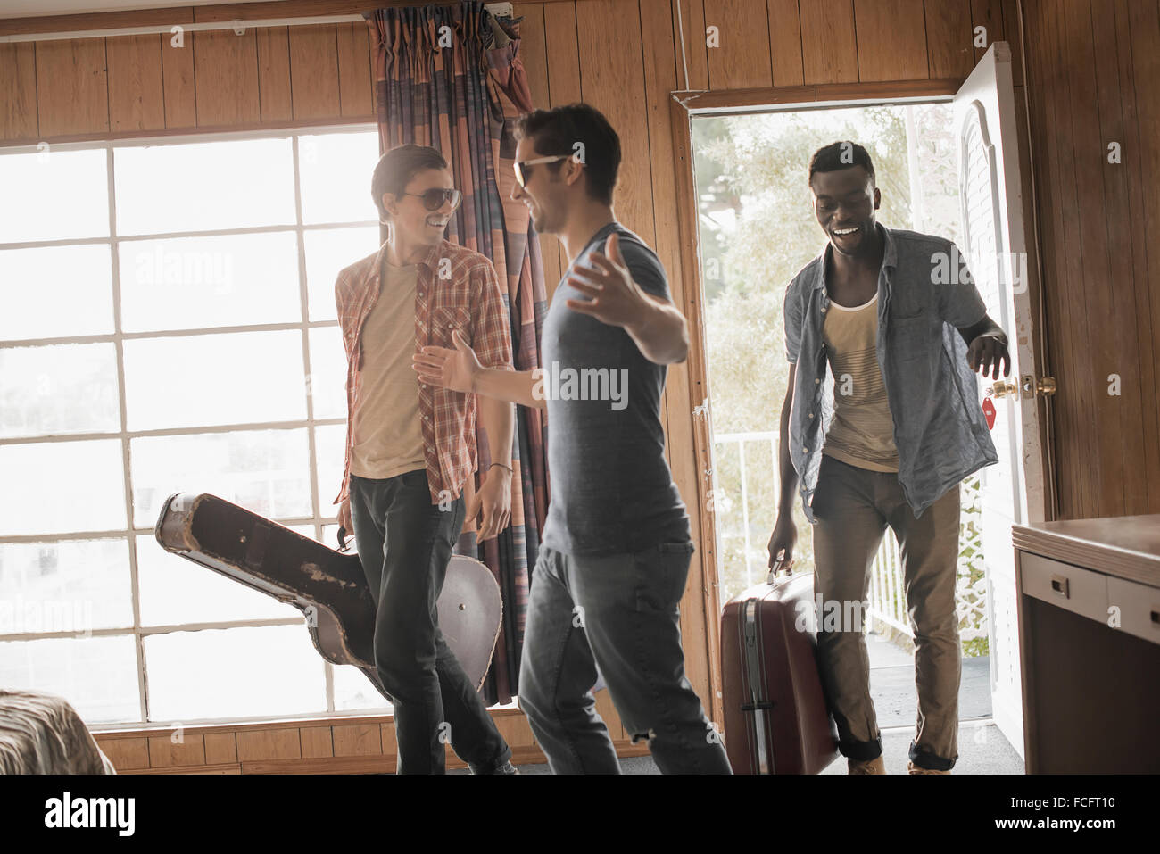 Freunde, drei junge Männer in einem Motelzimmer, Tragetaschen und eine Gitarre. Stockfoto