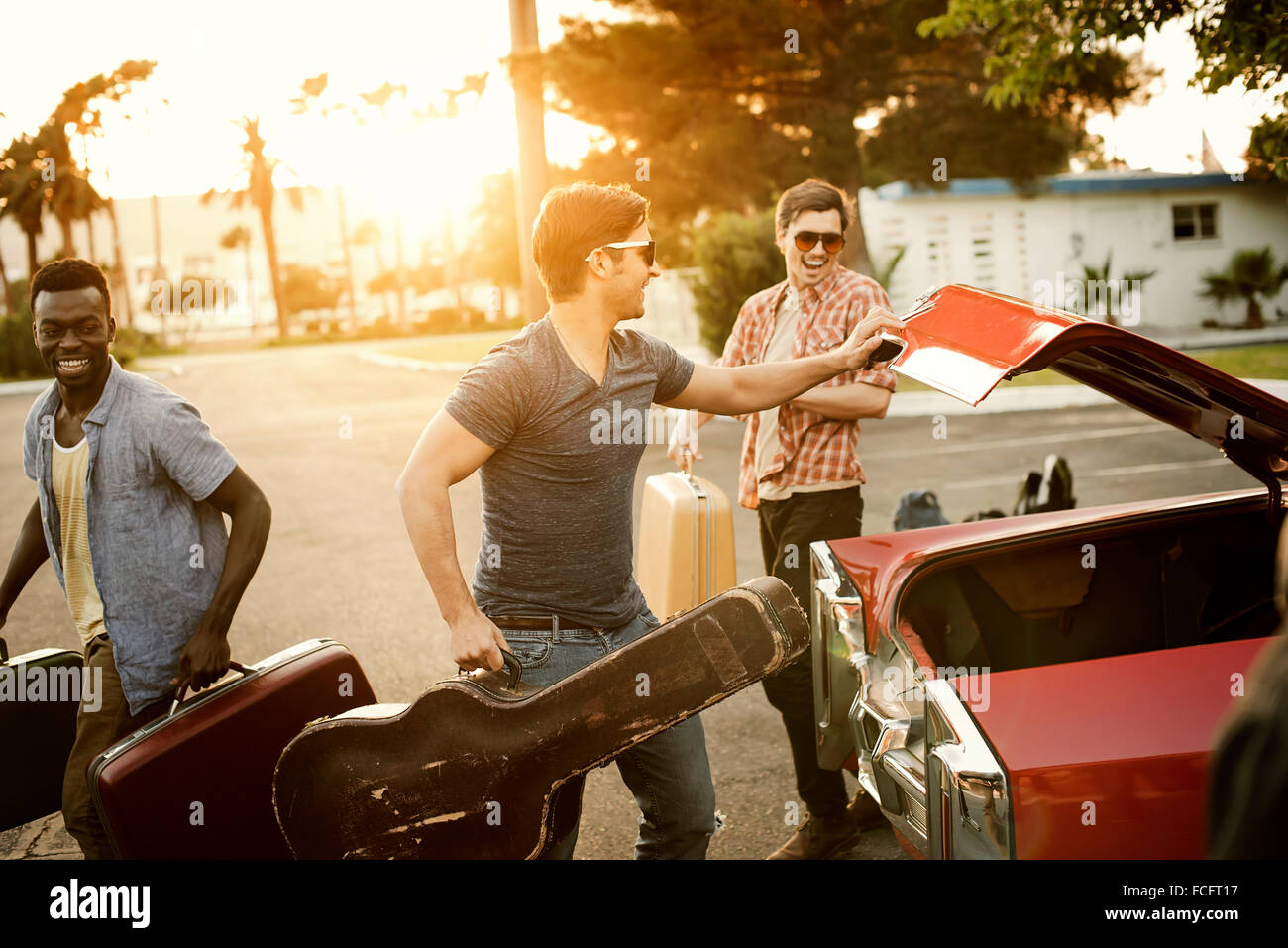 Drei junge Männer, Freunde, packen das Auto mit Koffer und eine Gitarre für einen Roadtrip. Stockfoto